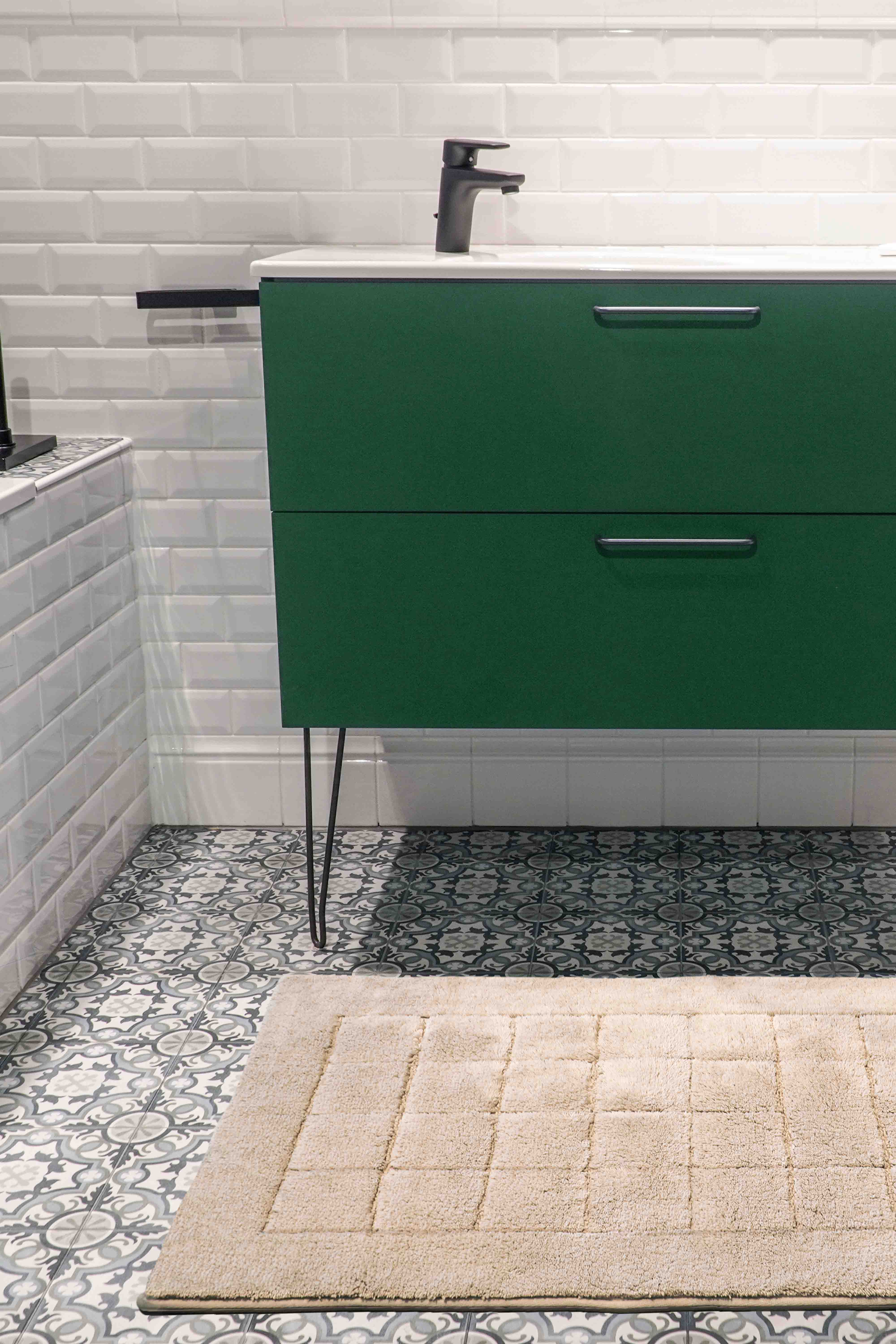 Beiger VOSSEN Badvorleger auf gemusterten Fliesen in modernem Badezimmer mit grüner Waschtischkommode und schwarzer Armatur – stilvolle Kombination aus Komfort und Design.