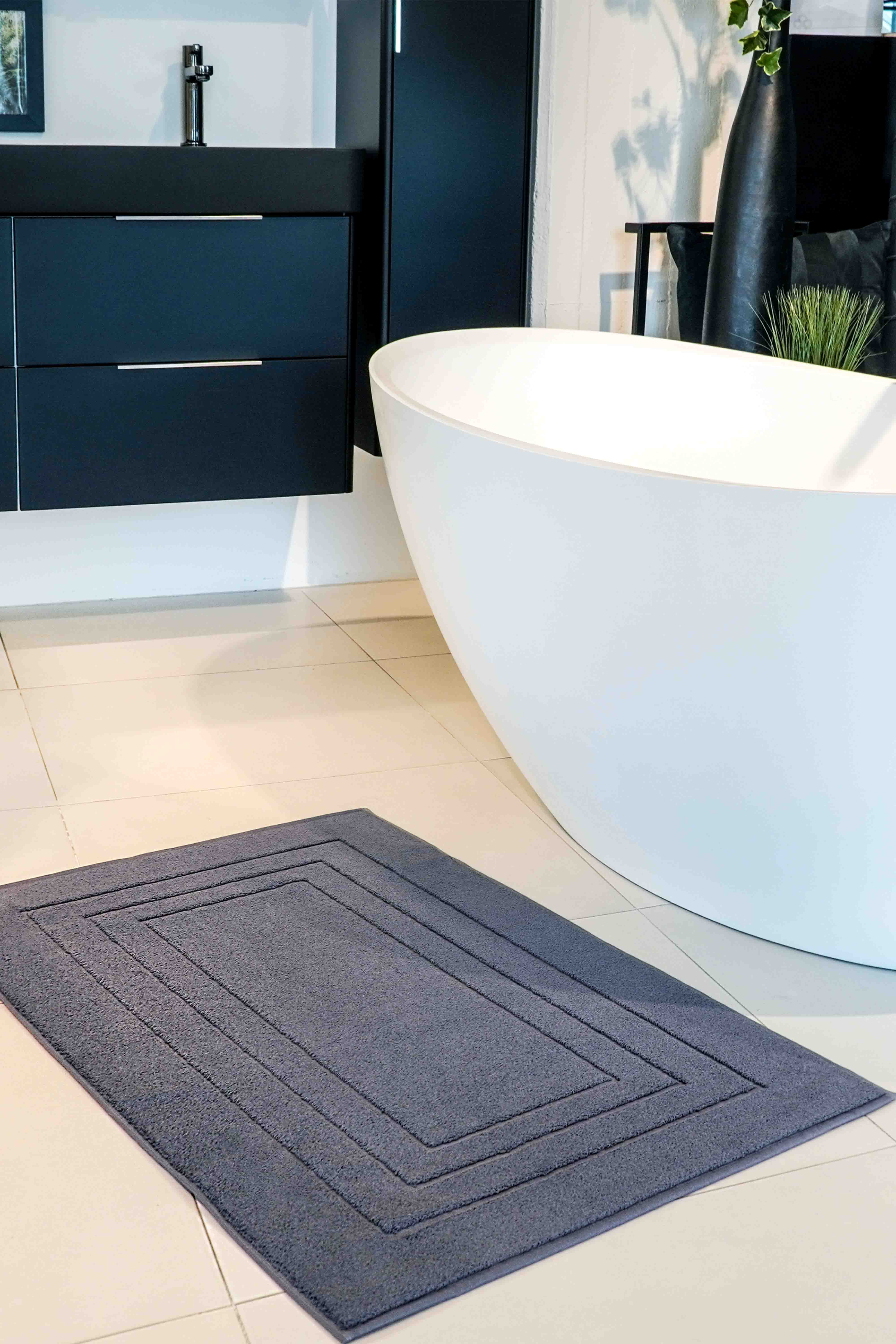 Dunkelgrauer VOSSEN Badteppich vor freistehender Badewanne in modernem Badezimmer mit schwarzem Waschtisch – stilvolles Badaccessoire für elegantes Interior Design.