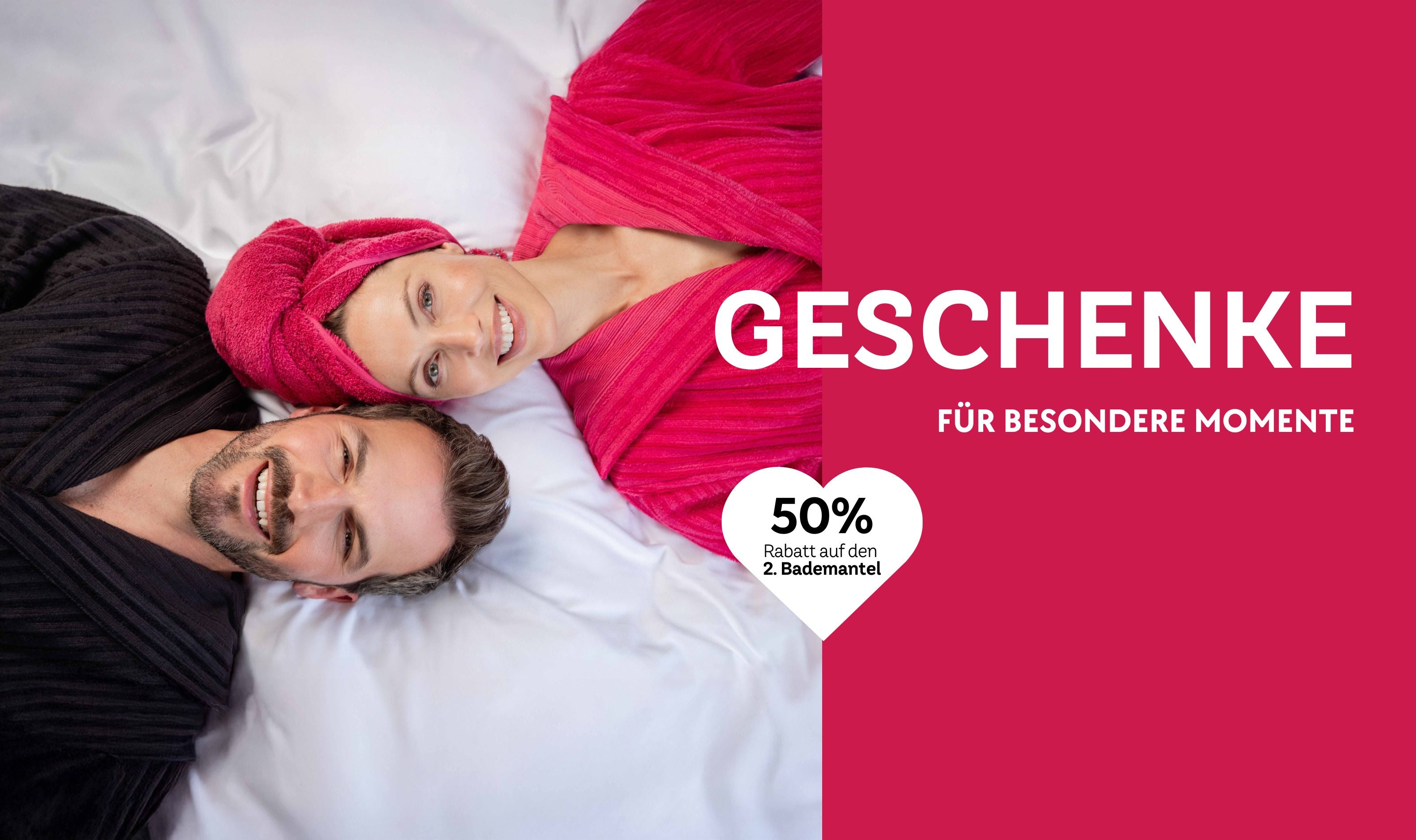 Paar in VOSSEN Bademänteln liegt entspannt auf weißer Bettwäsche, Geschenkaktion mit 50 % Rabatt auf den zweiten Bademantel – Geschenkideen für besondere Momente.