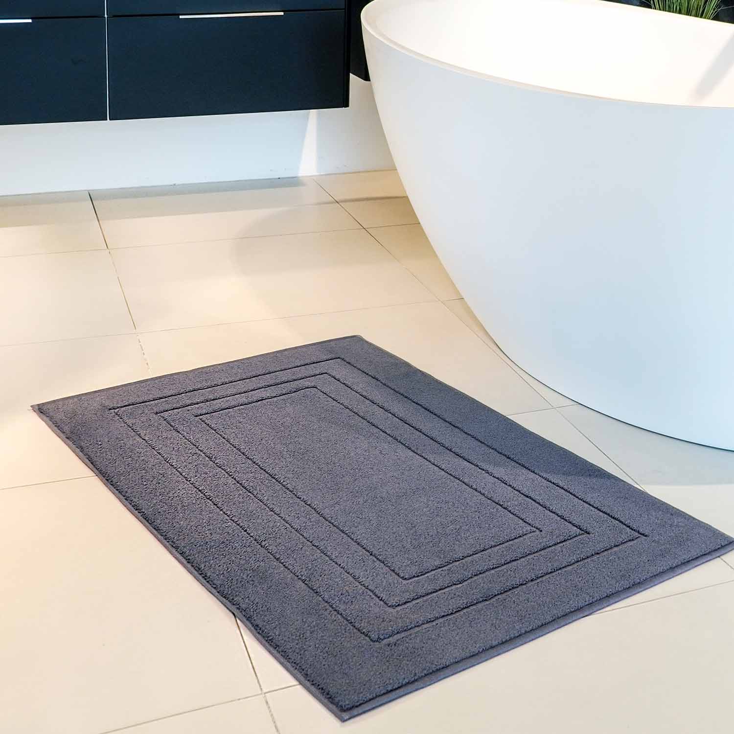 Modernes Badezimmer mit freistehender weißer Badewanne, Chromarmatur und dunkelgrauer Badematte auf dem Boden.