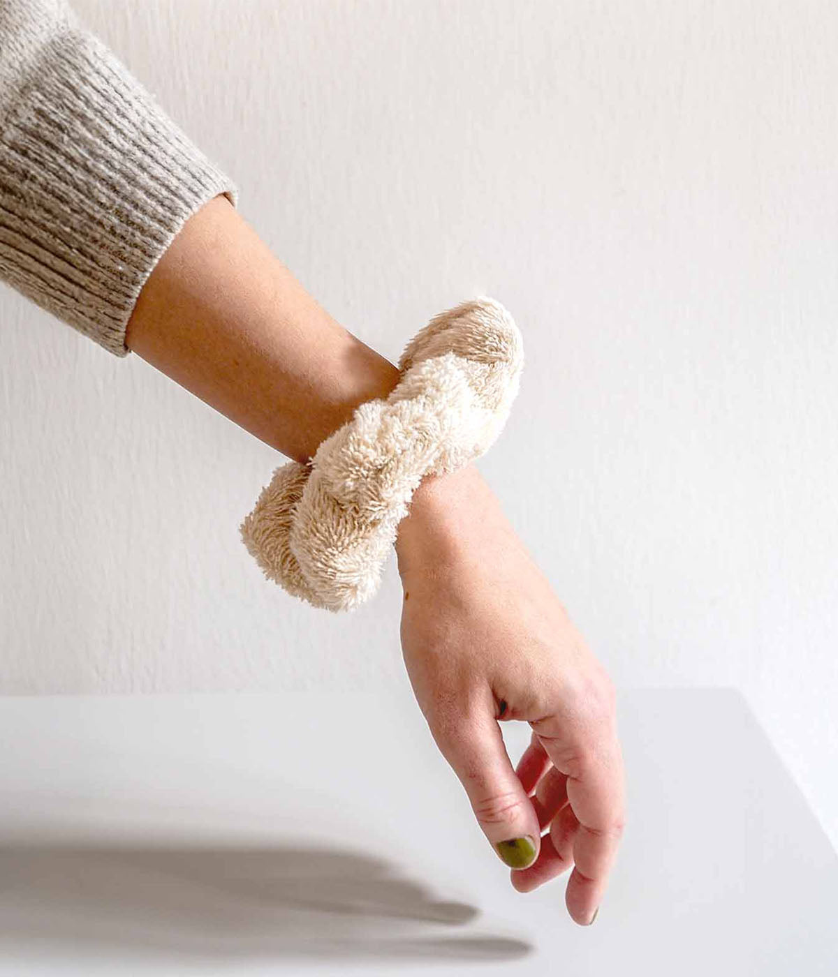 Ausgestreckter Arm mit beigem Scrunchie vor hellem Hintergrund.