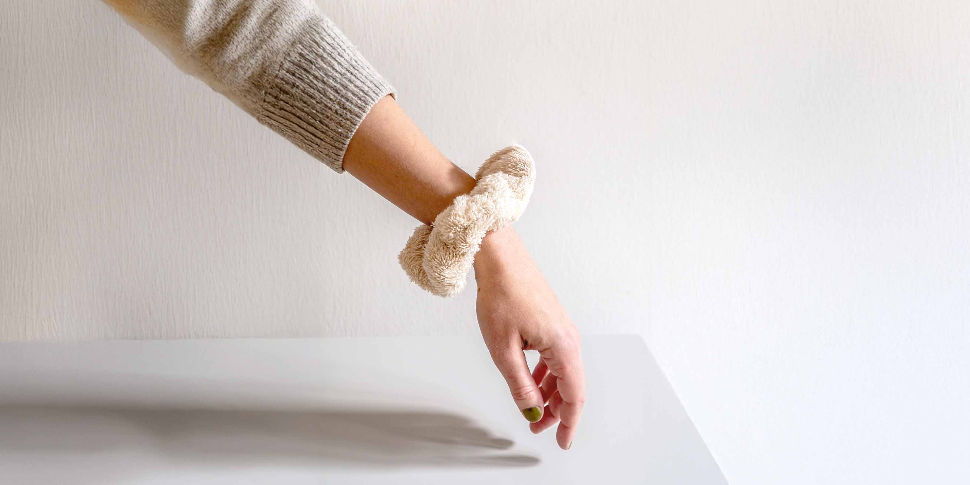 Ausgestreckter Arm mit beigem Scrunchie vor hellem Hintergrund.