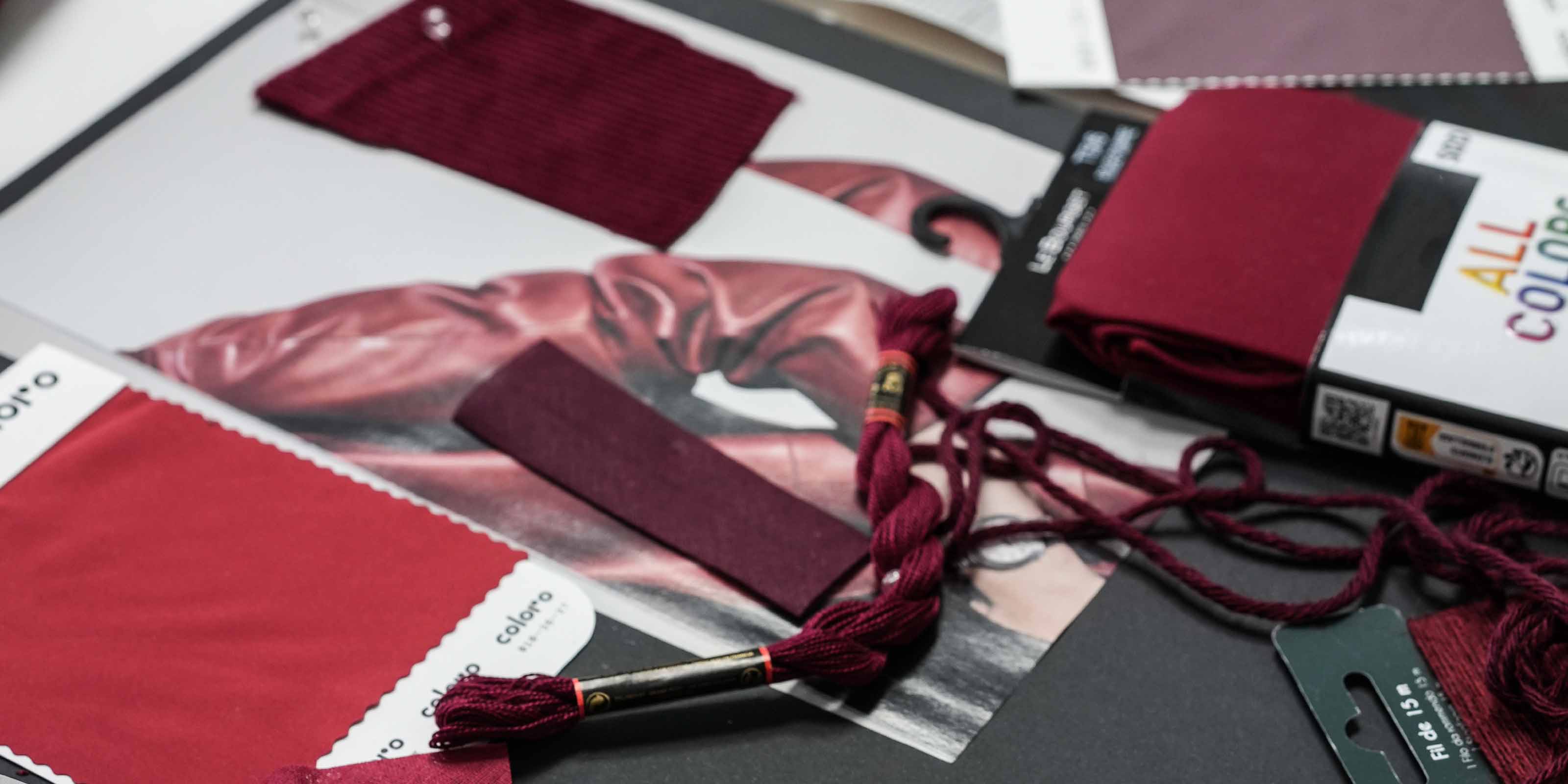 Nahaufnahme eines Moodboards mit verschiedenen Stoffmustern, Garnproben und Farbkarten in Rottönen – von dunklem Bordeaux bis zu hellem Rosé – arrangiert auf schwarzem Untergrund.