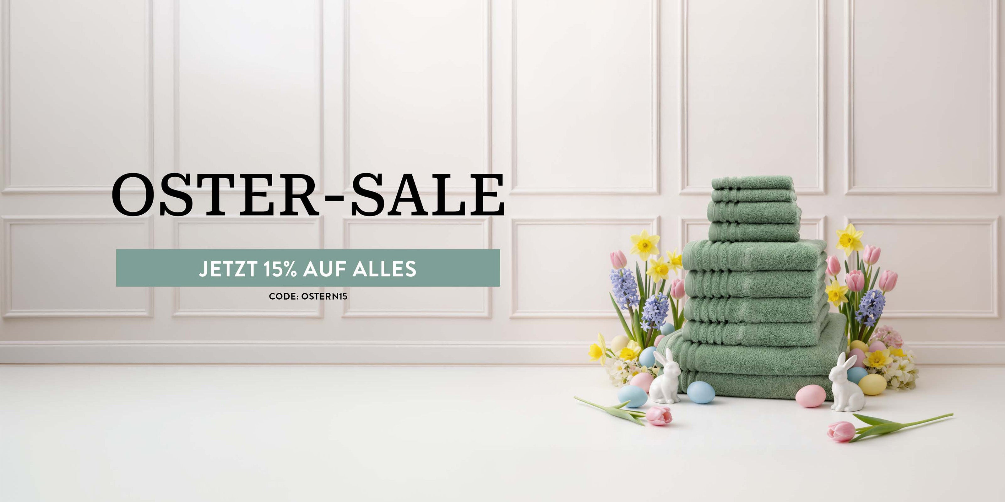 Stapel grüner Handtücher mit Osterdekoration und Text ‚Oster-Sale – 15% auf alles