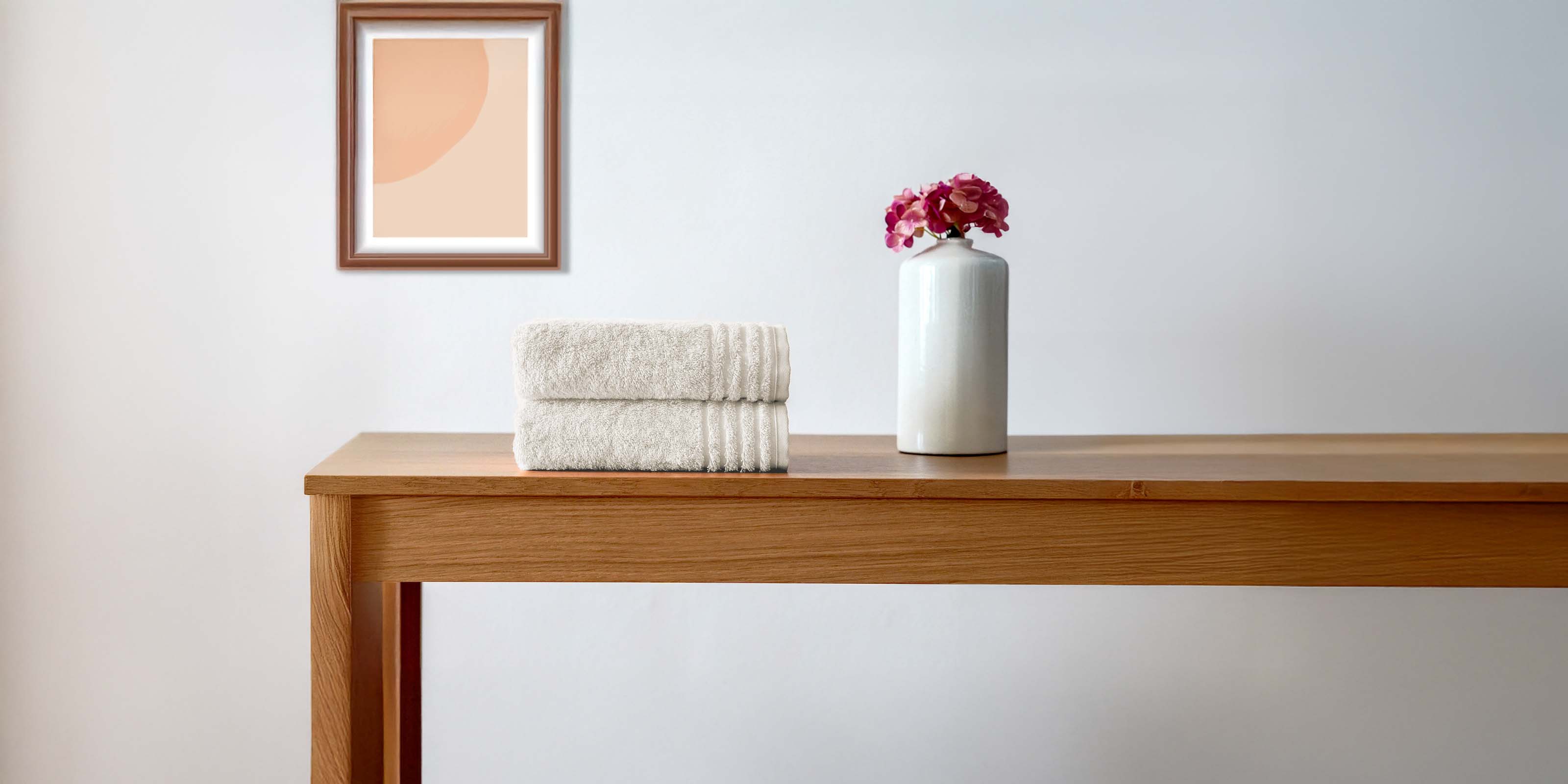 Zwei gefaltete cremefarbene VOSSEN Handtücher aus weicher Baumwolle auf Holztisch – stilvolle Badtextilien für modernes Interior Design.