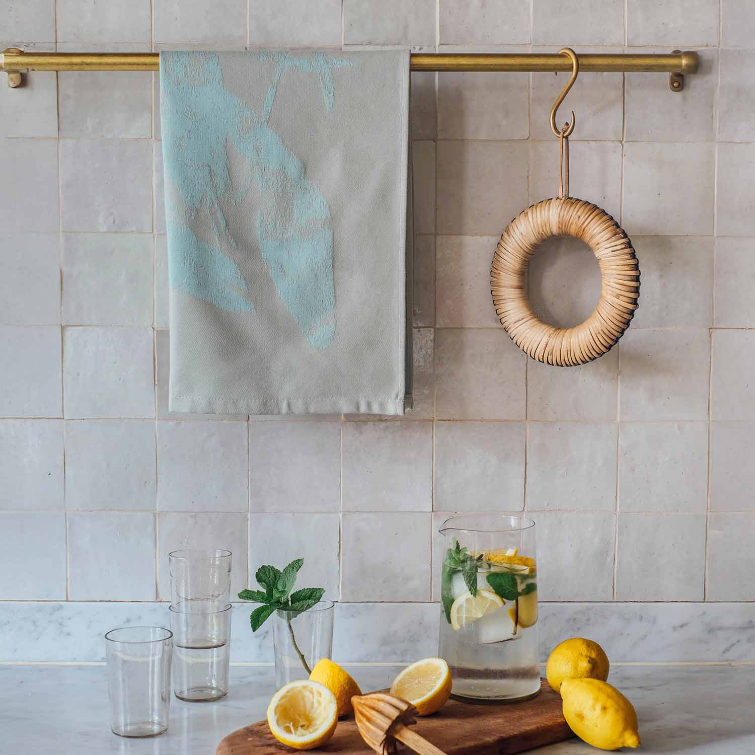 Modernes Geschirrtuch in Mintgrün an goldener Küchenstange, darunter Zitronen und Glas mit Zitronenwasser auf Arbeitsplatte