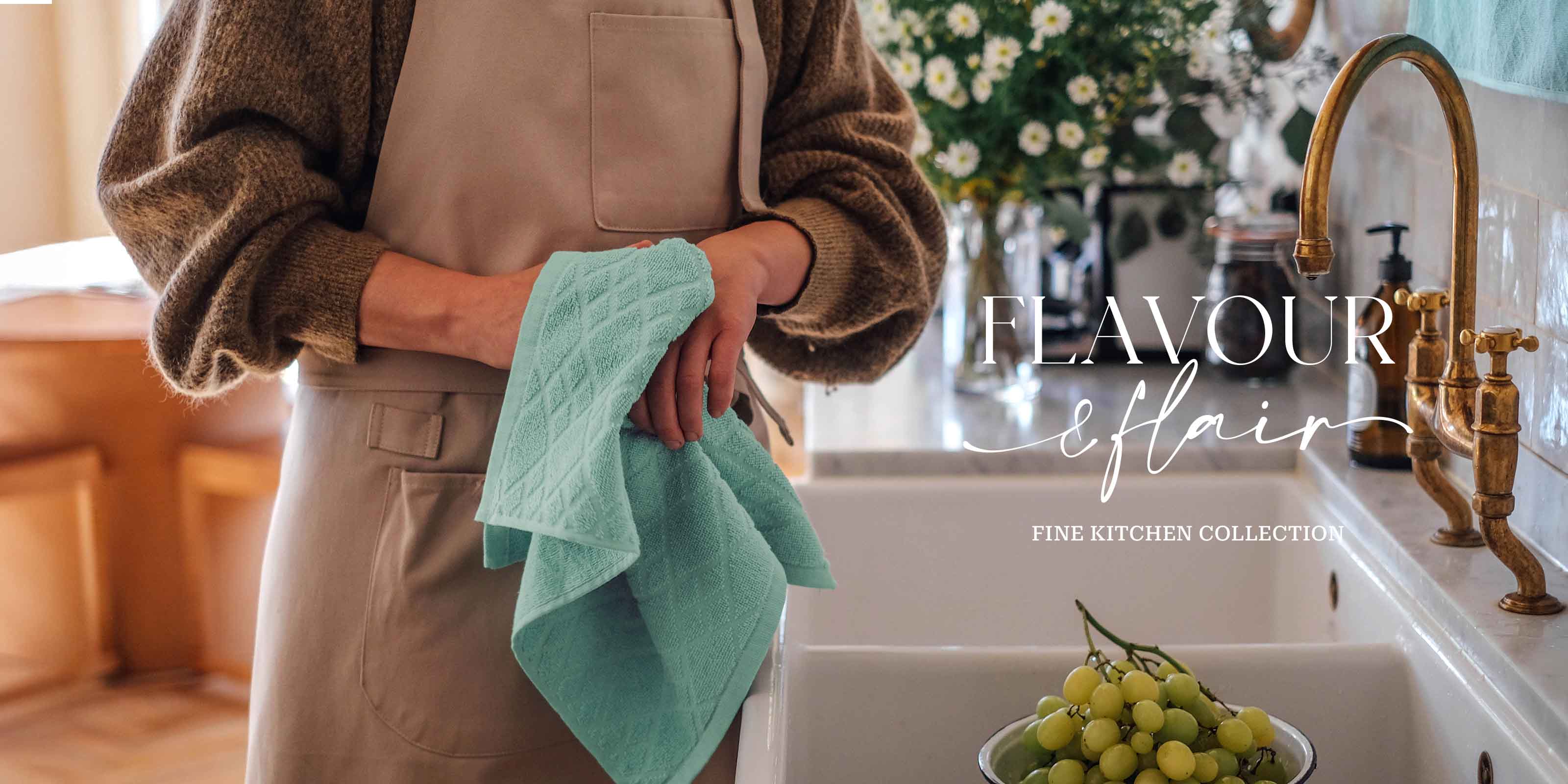 Person mit Küchenschürze hält ein türkisfarbenes Geschirrtuch am Spülbecken – Flavour Flair Fine Kitchen Collection