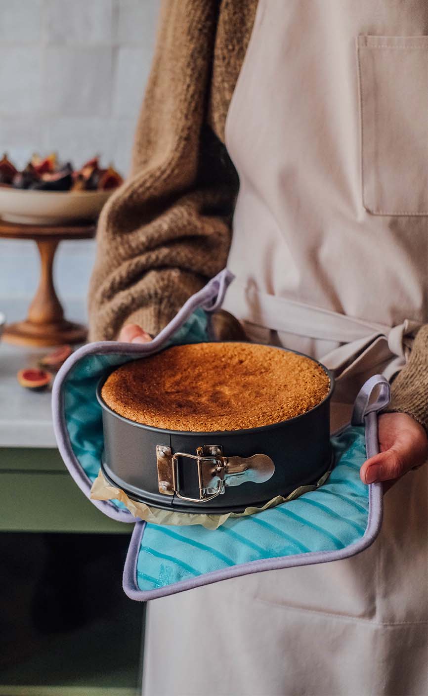 Frisch gebackener Kuchen in einer Springform, gehalten mit Ofenhandschuhen in der Küche – goldbrauner Kuchen nach dem Backen