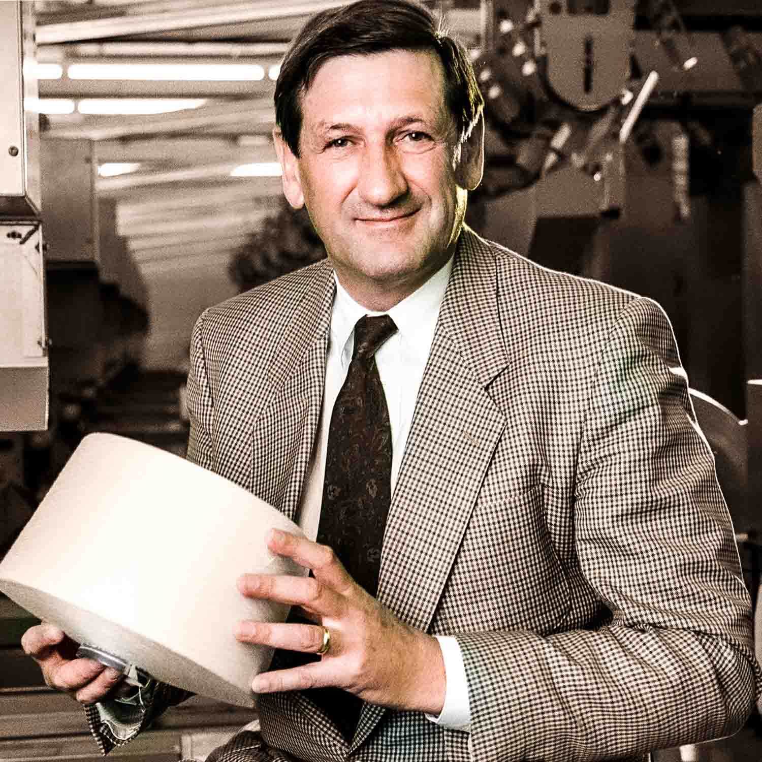 Älterer Mann hält lächelnd eine Garnspule in den Händen.