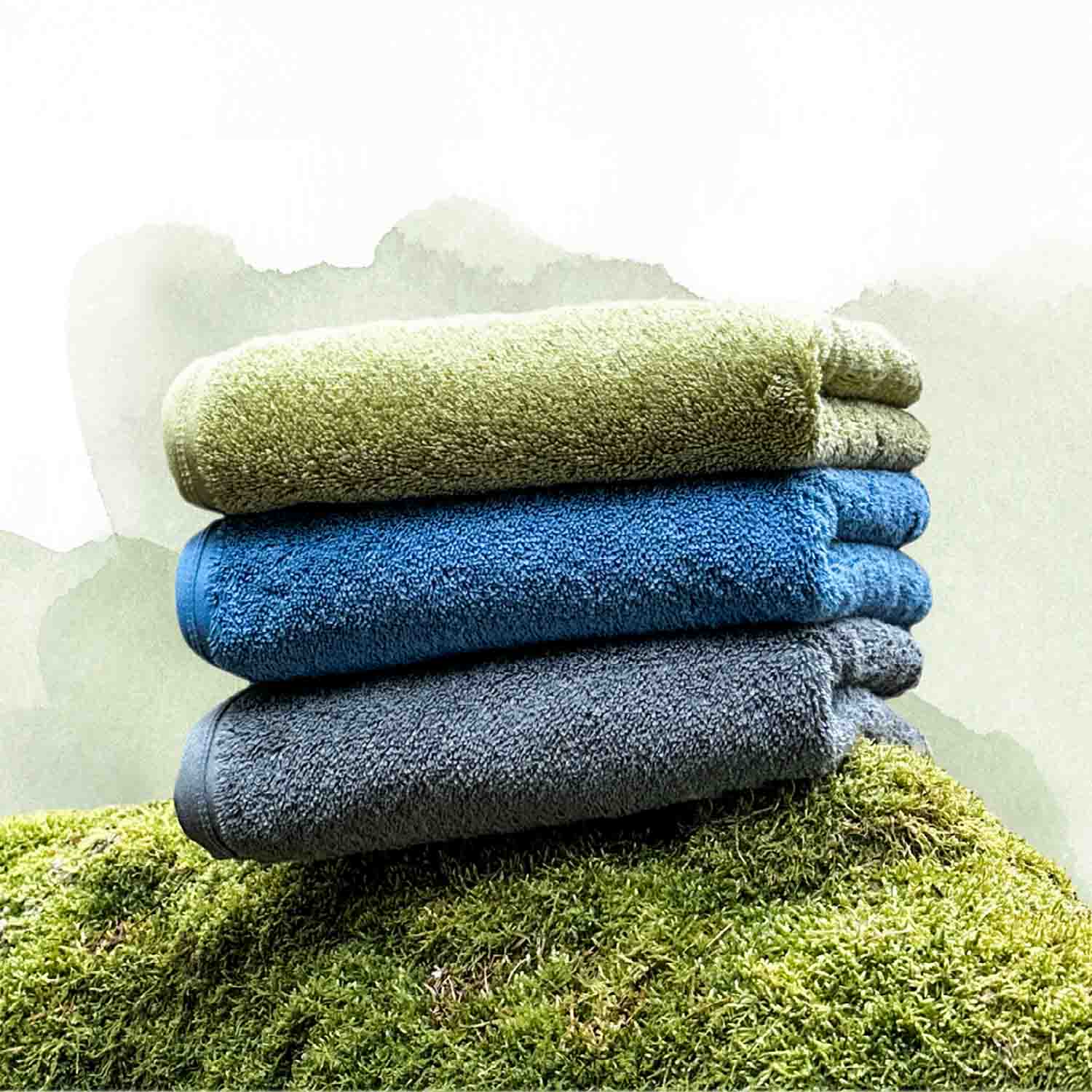 Handtuchstapel in den Farben Grün, Blau und Grau liegt schön geordnet auf einem Moosbett.