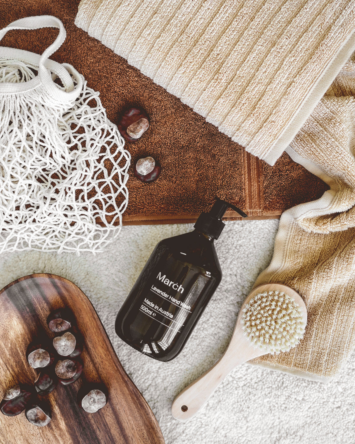 Flach gelegte Wellness-Accessoires mit Handtüchern in Naturtönen, Massagebürste, Lavendel-Handseife, Kastanien und Netzbeutel für ein natürliches Spa-Gefühl.