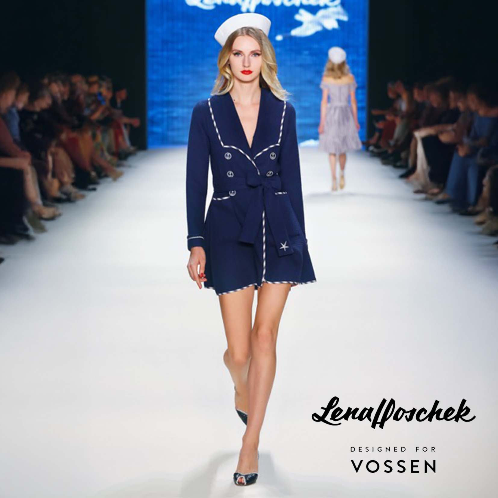 Model auf einem Laufsteg trägt ein marineblaues Outfit mit weißem Besatz und Matrosenmütze. Im Hintergrund ein weiteres Model in ähnlichem Stil. Publikum sitzt beidseitig. Unten rechts steht: ‚Lena Hoschek – DESIGNED FOR VOSSEN‘.