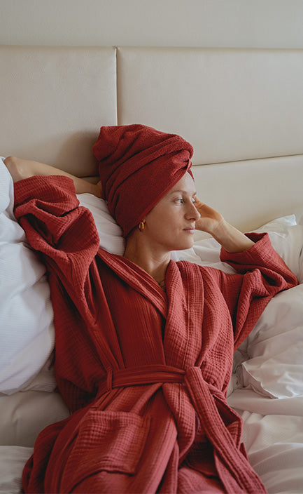 Person in rotem Bademantel und dazu passender roter Turban liegt auf einem Bett.