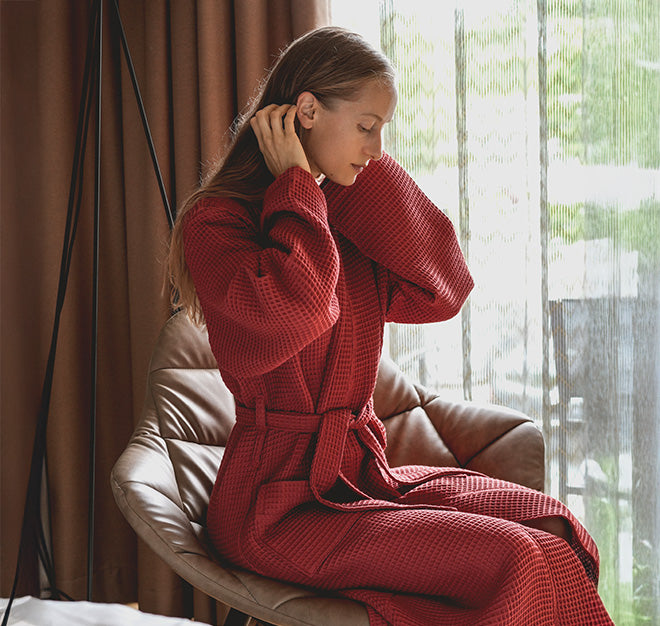 Person in rotem Bademantel sitzt auf einem Sessel und streicht sich die Haare zurück.