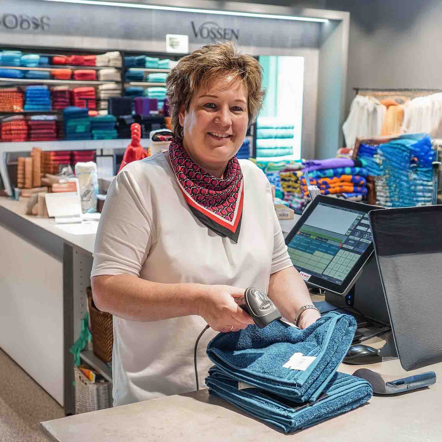 Freundliche Verkäuferin scannt Handtücher an der Kasse in einem gut sortierten VOSSEN-Store.