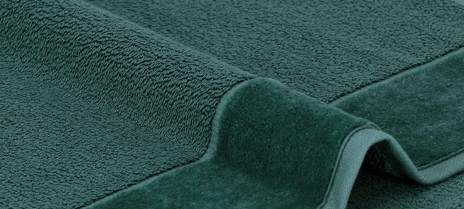 Nahaufnahme eines dunkelgrünen Handtuchs mit strukturierter Oberfläche und gefalteten Kanten.