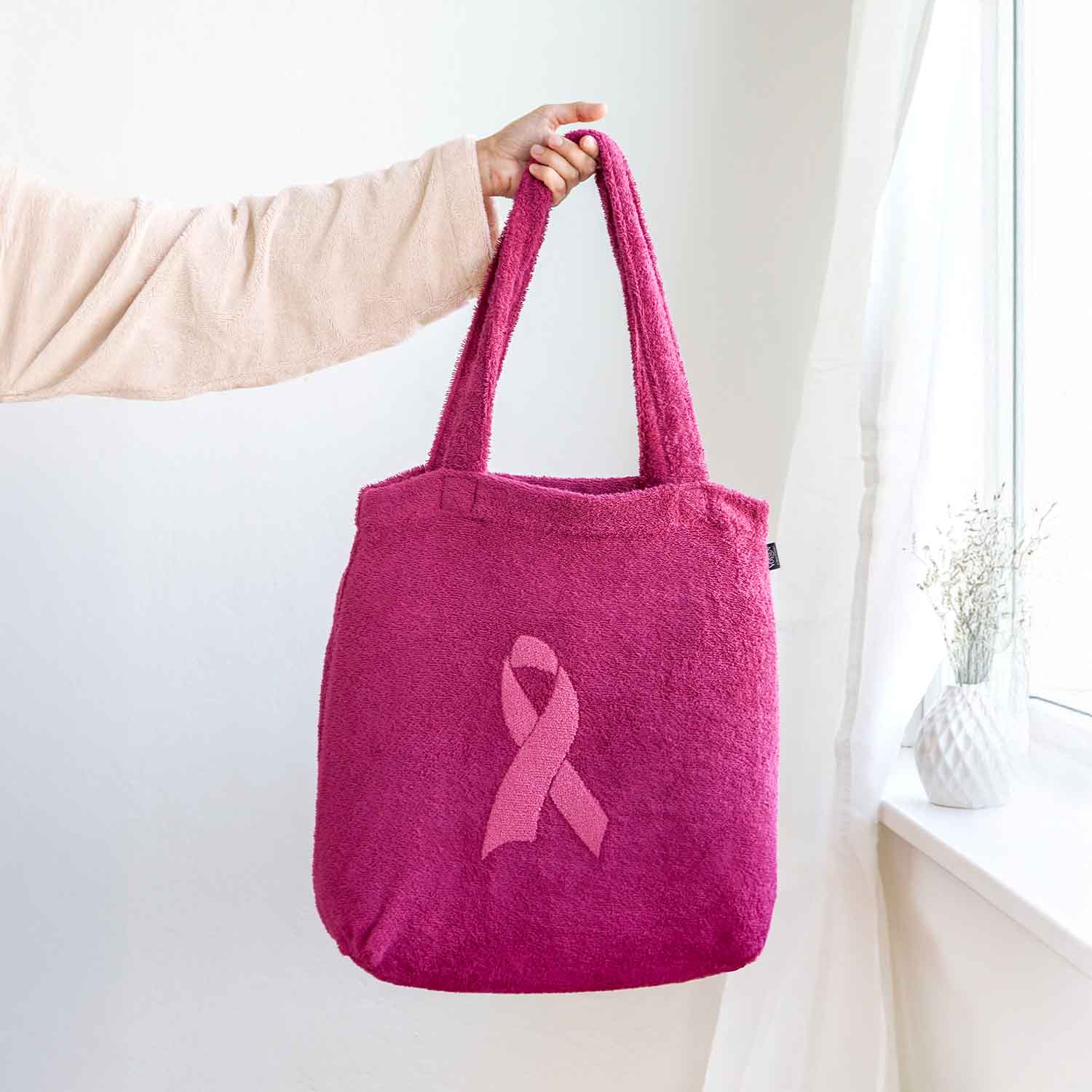 Frau hält eine pinke Tasche aus Frottee mit eingestickter Brustkrebsschleife als Symbol für Solidarität und Unterstützung.