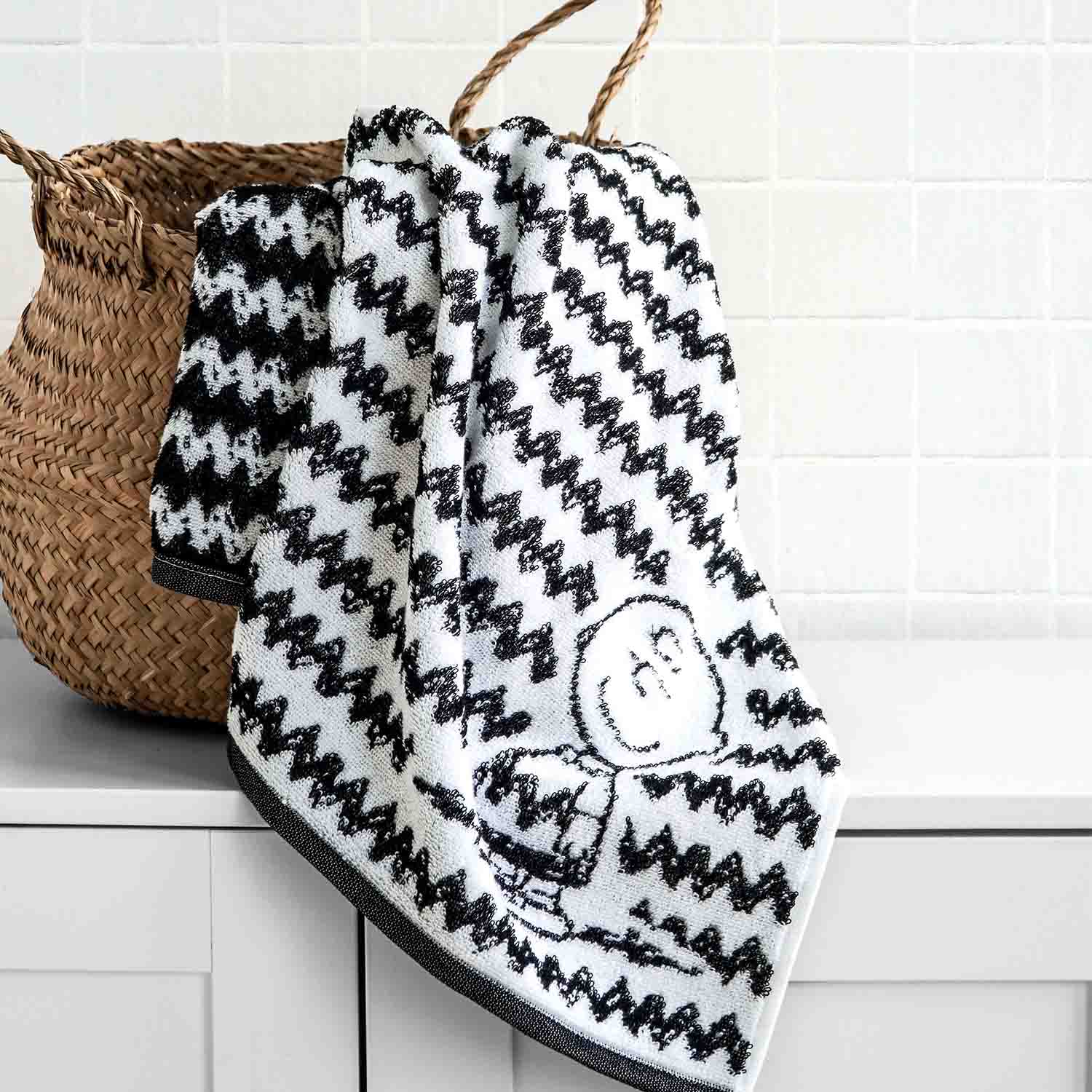 Schwarz-weiß gemustertes Handtuch mit Snoopy-Motiv hängt an einem Korb – stilvolles VOSSEN x Peanuts Design für Bad und Wellness.