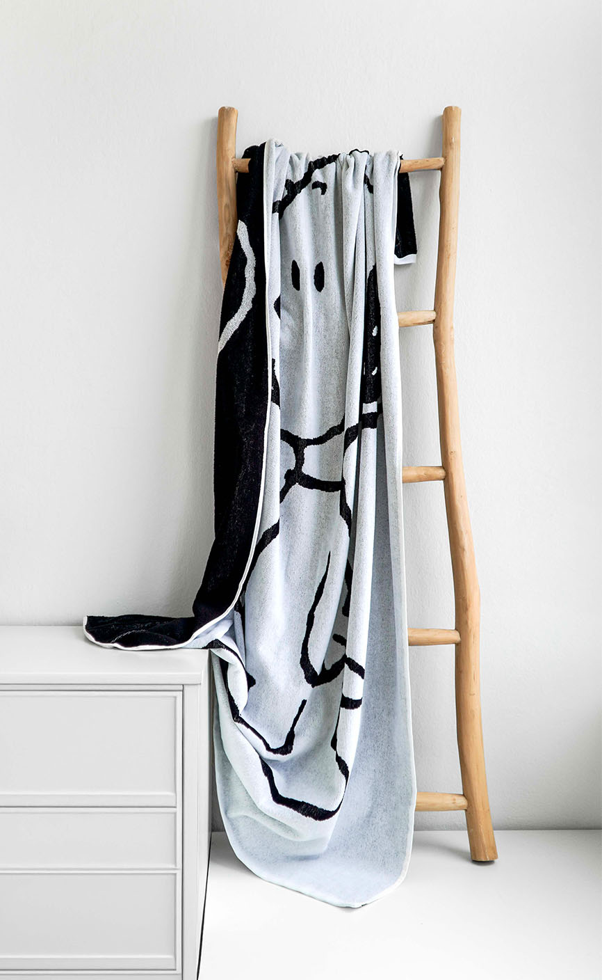 Hellgraues Handtuch mit Snoopy-Motiv hängt dekorativ an einer Holzleiter in modernem, minimalistischen Raum – Teil der VOSSEN x Peanuts Kollektion.