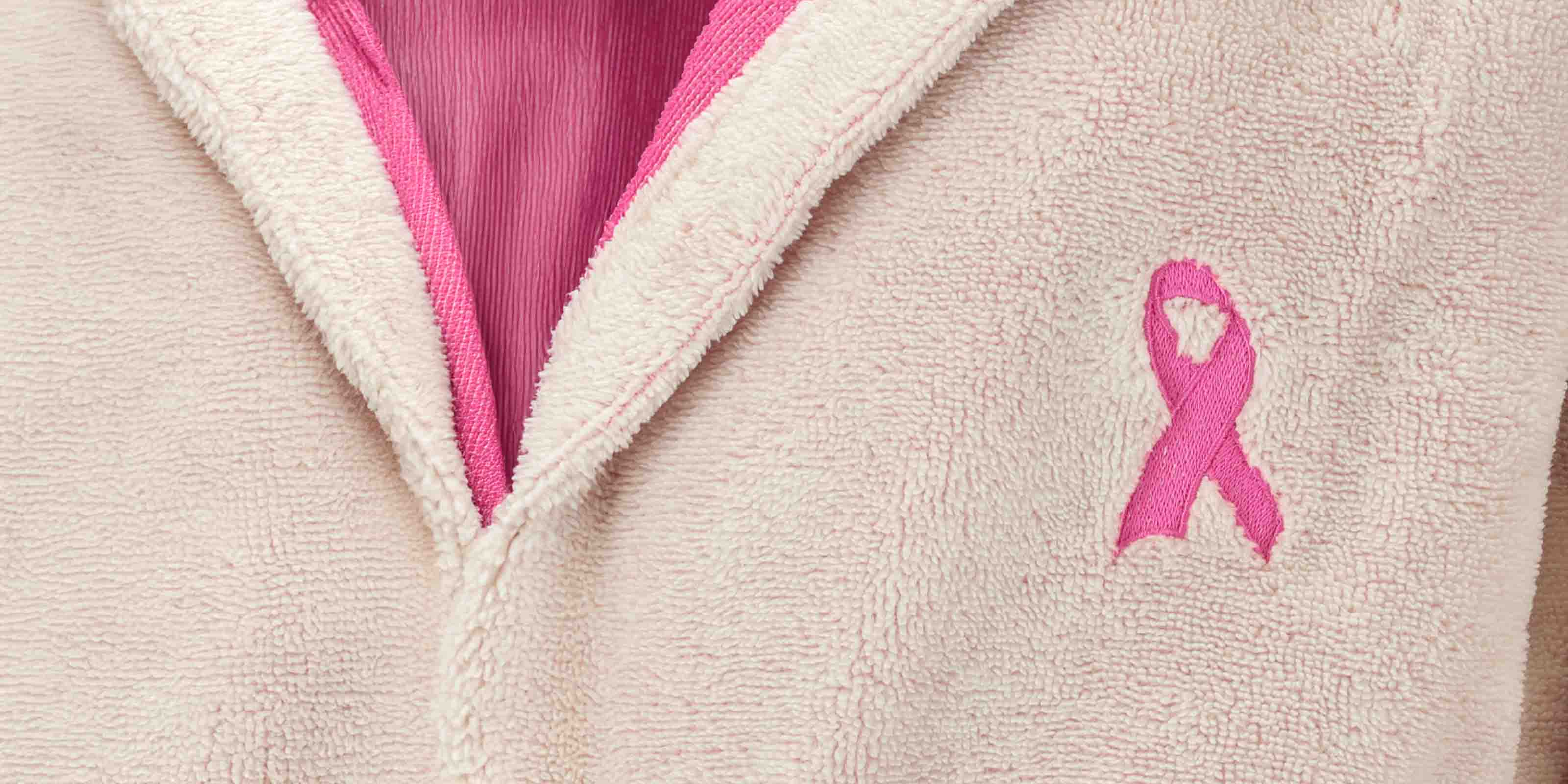 Beiger Bademantel mit pinkem Innenfutter und eingestickter Brustkrebsschleife als Symbol für Bewusstsein und Unterstützung.