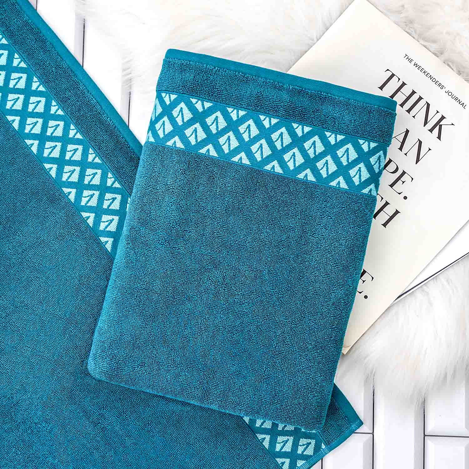 Gefaltetes blaues Handtuch mit Borteneinwebung auf ausgebreitetem Tuch, dahinter Magazin.