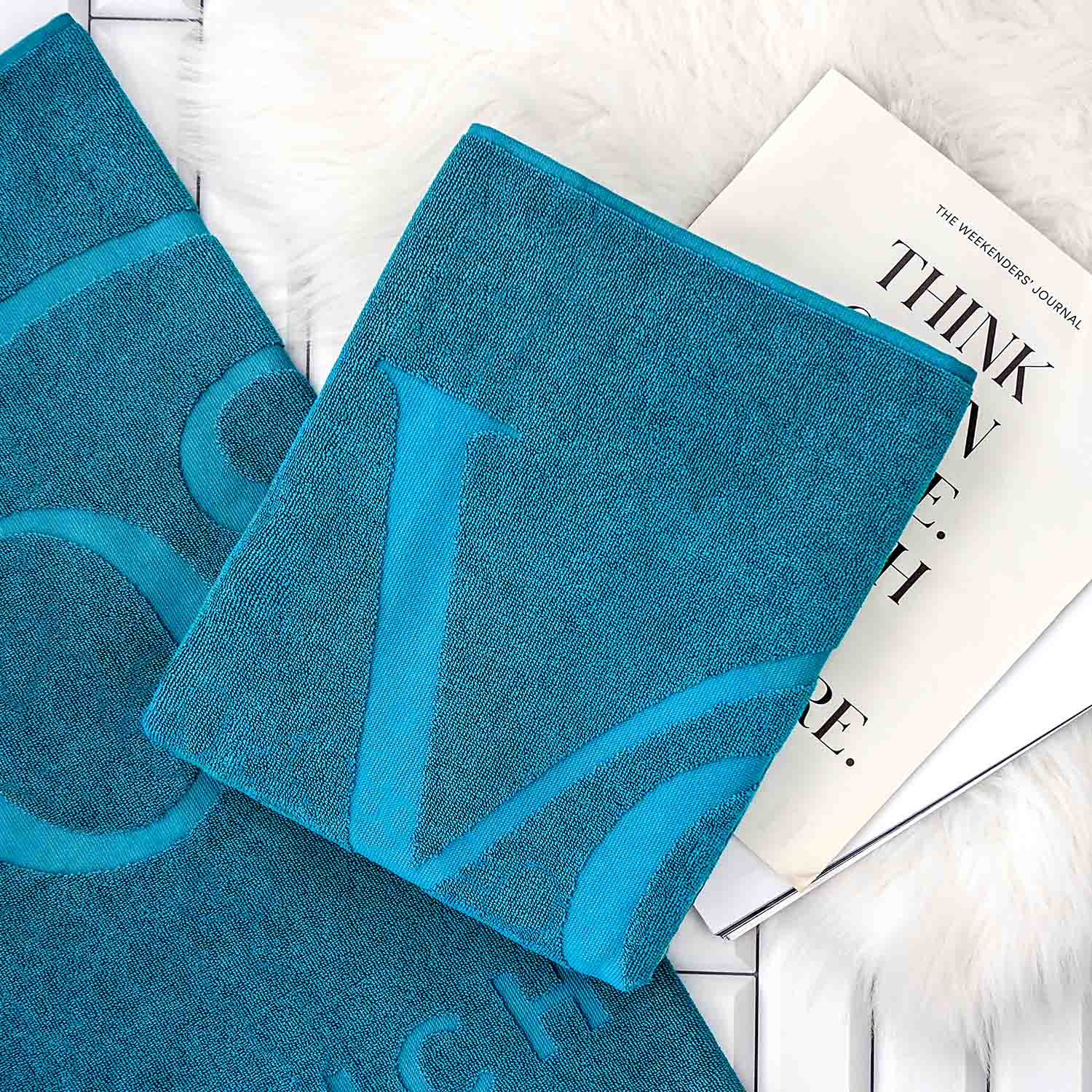 Gefaltetes blaues Handtuch mit Reliefeinwebung auf ausgebreitetem Tuch, dahinter Magazin.