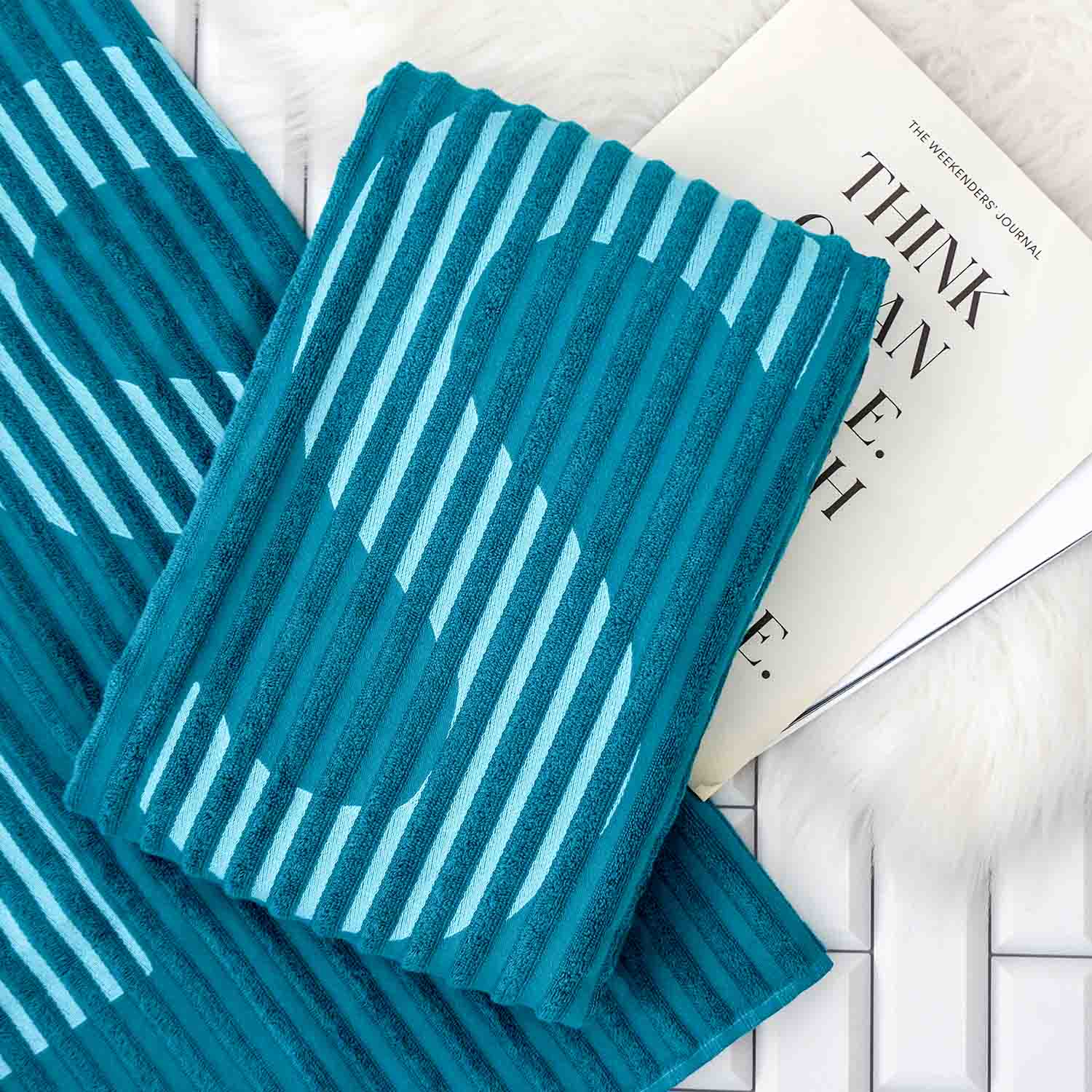 Gefaltetes blaues Handtuch mit Welleneinwebung auf ausgebreitetem Tuch, dahinter Magazin.