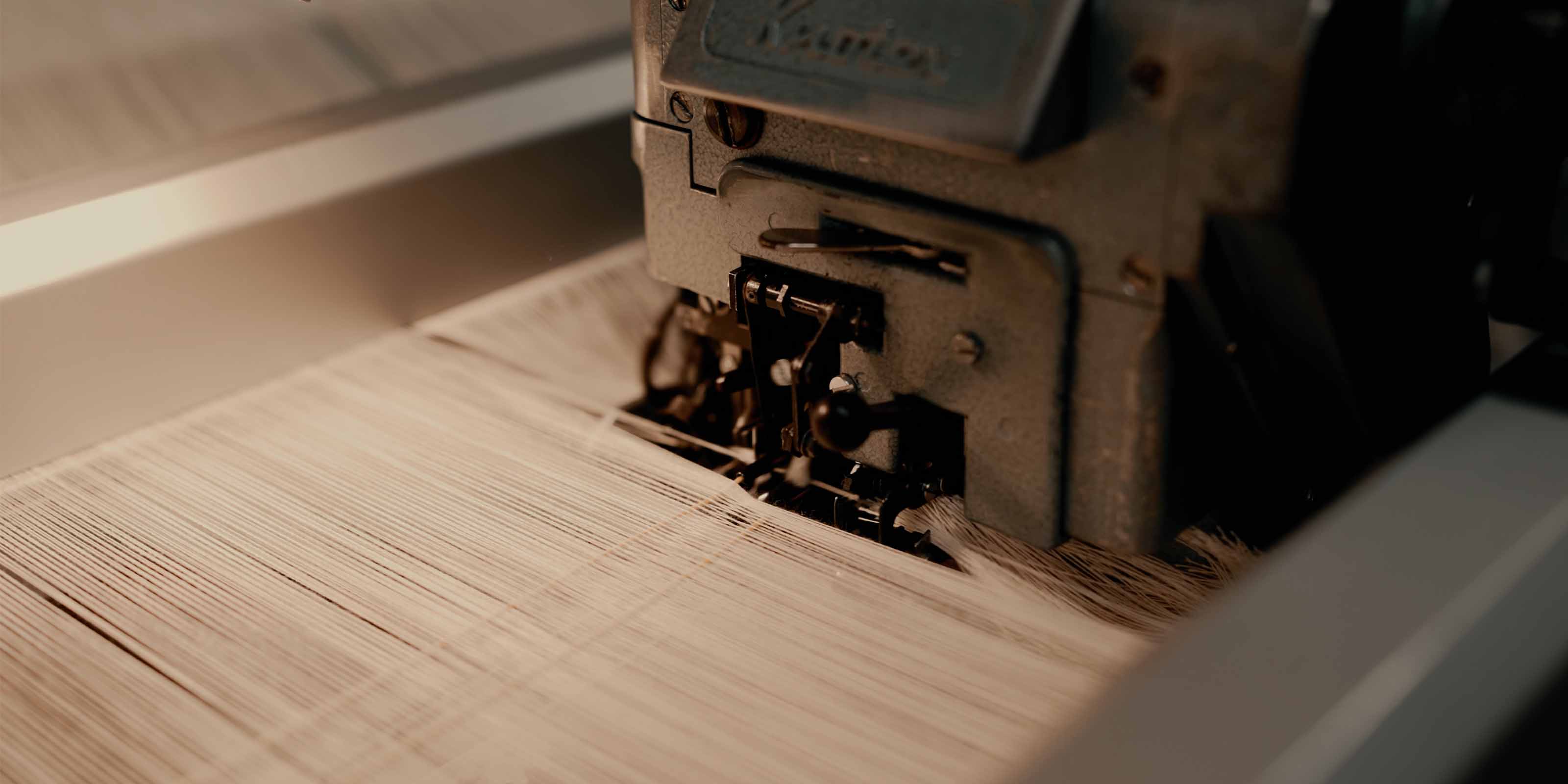 Detailaufnahme einer industriellen Webmaschine beim Verarbeiten von feinen Garnfäden während des Webvorgangs.