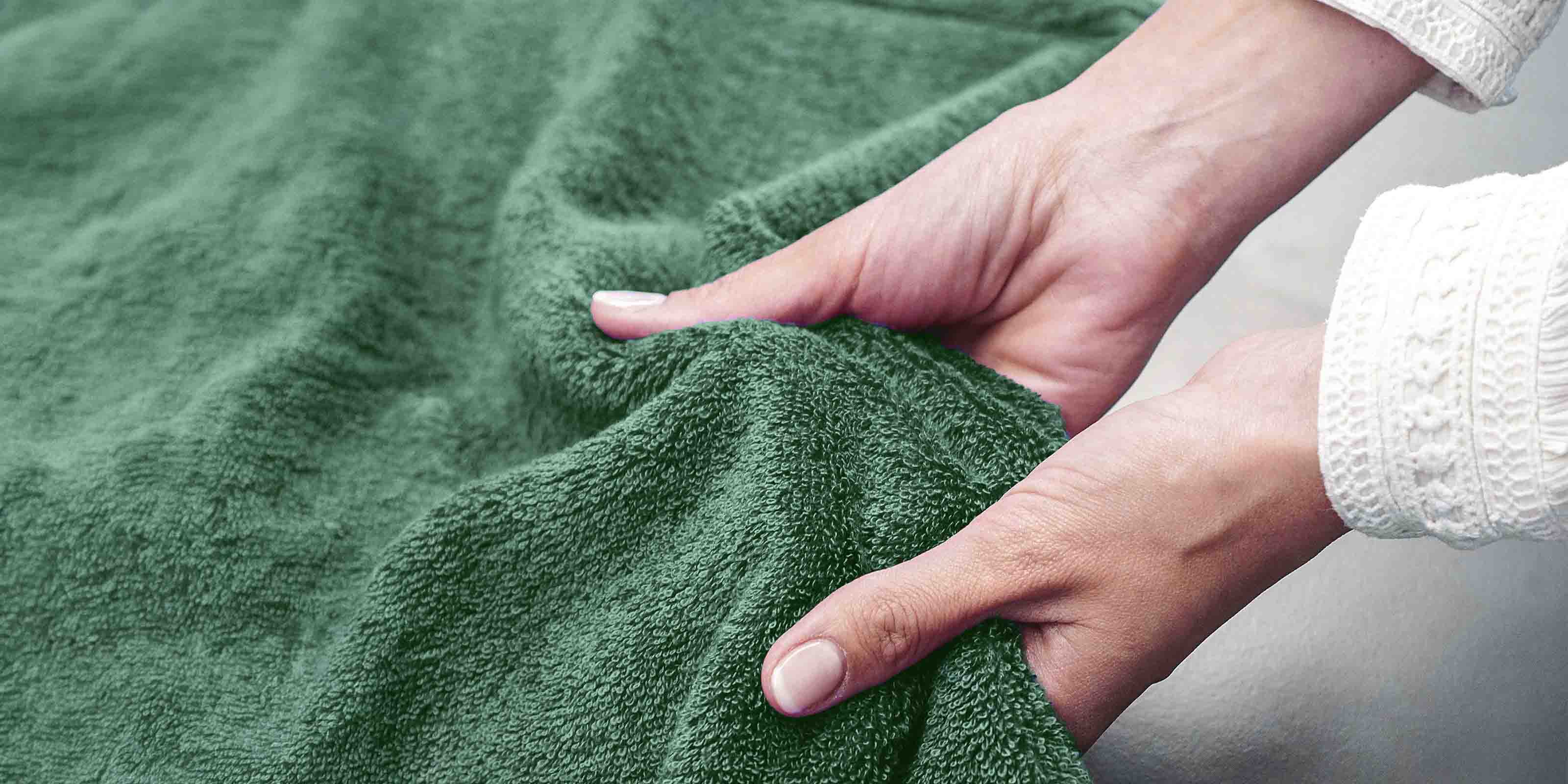 Zwei Hände greifen in ein grünes Frottierhandtuch und zeigen dessen weiche Struktur.