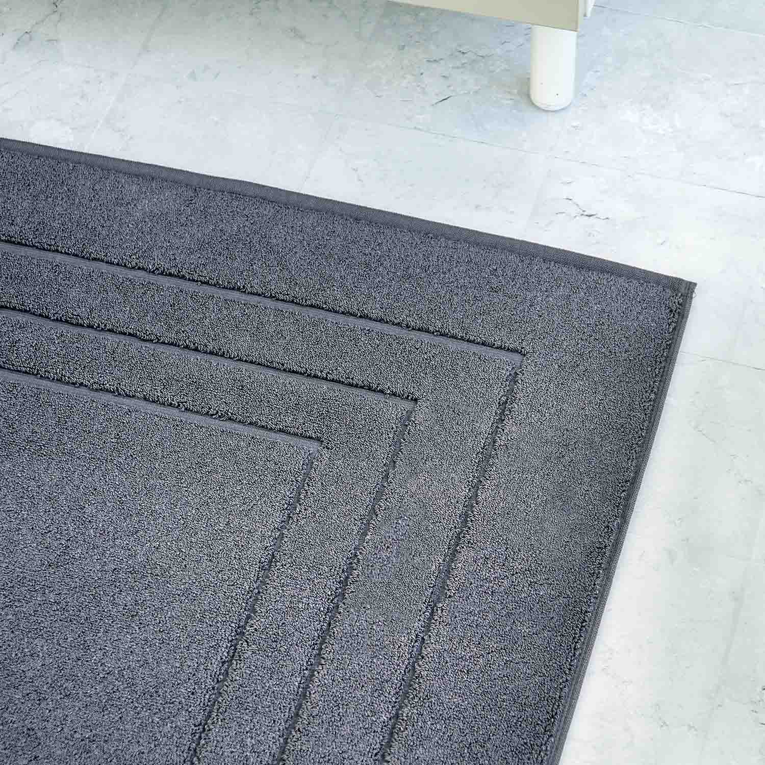 Grauer Teppich mit geometrischem Muster auf hellem Fliesenboden.