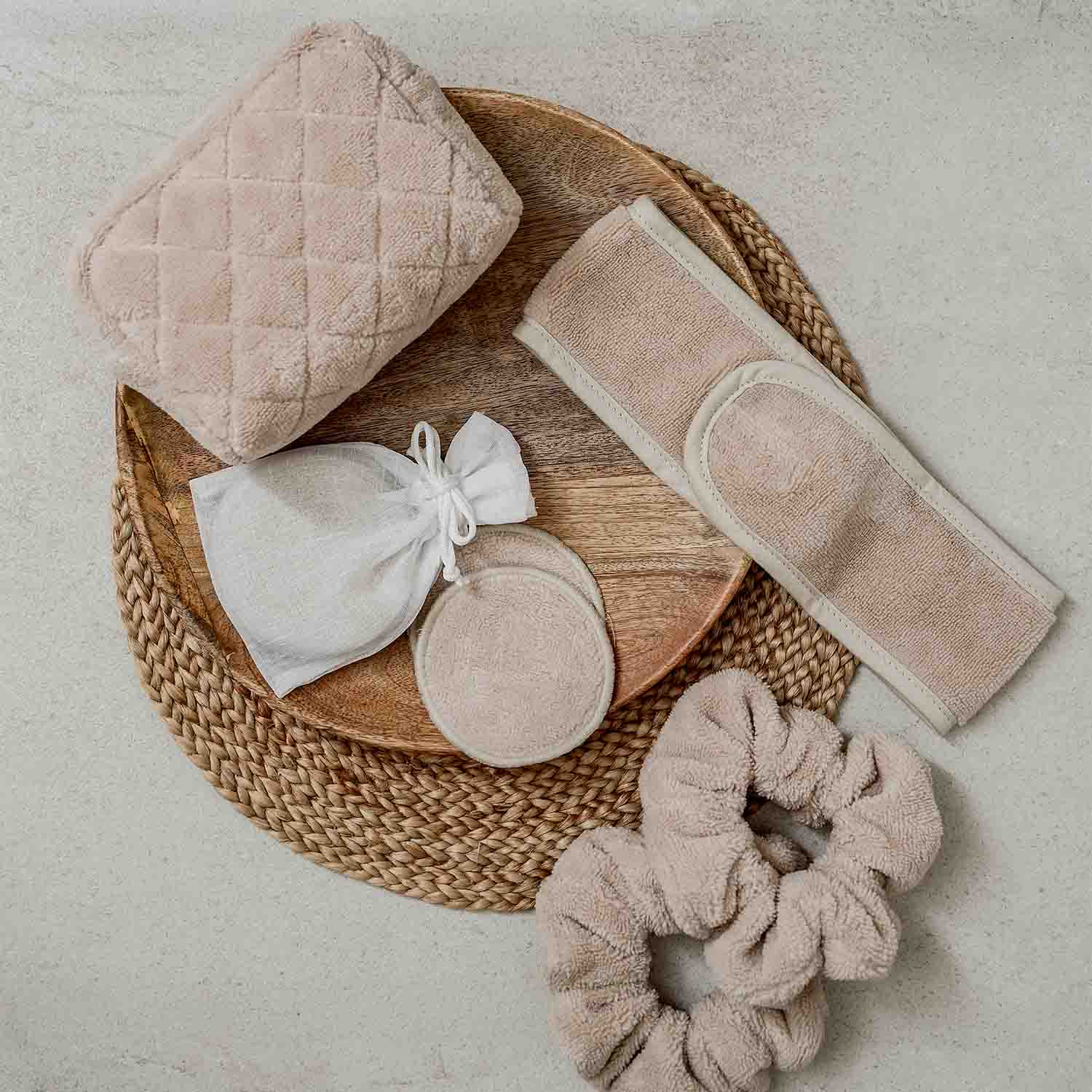 Beige Wellness-Accessoires wie Handtuch, wiederverwendbare Abschminkpads und Kosmetiktäschchen auf Holztablett.