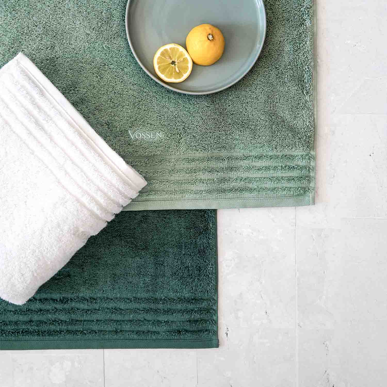 Zwei grüne und ein weißes Handtuch mit Zitrone auf Teller, Marke VOSSEN sichtbar.
