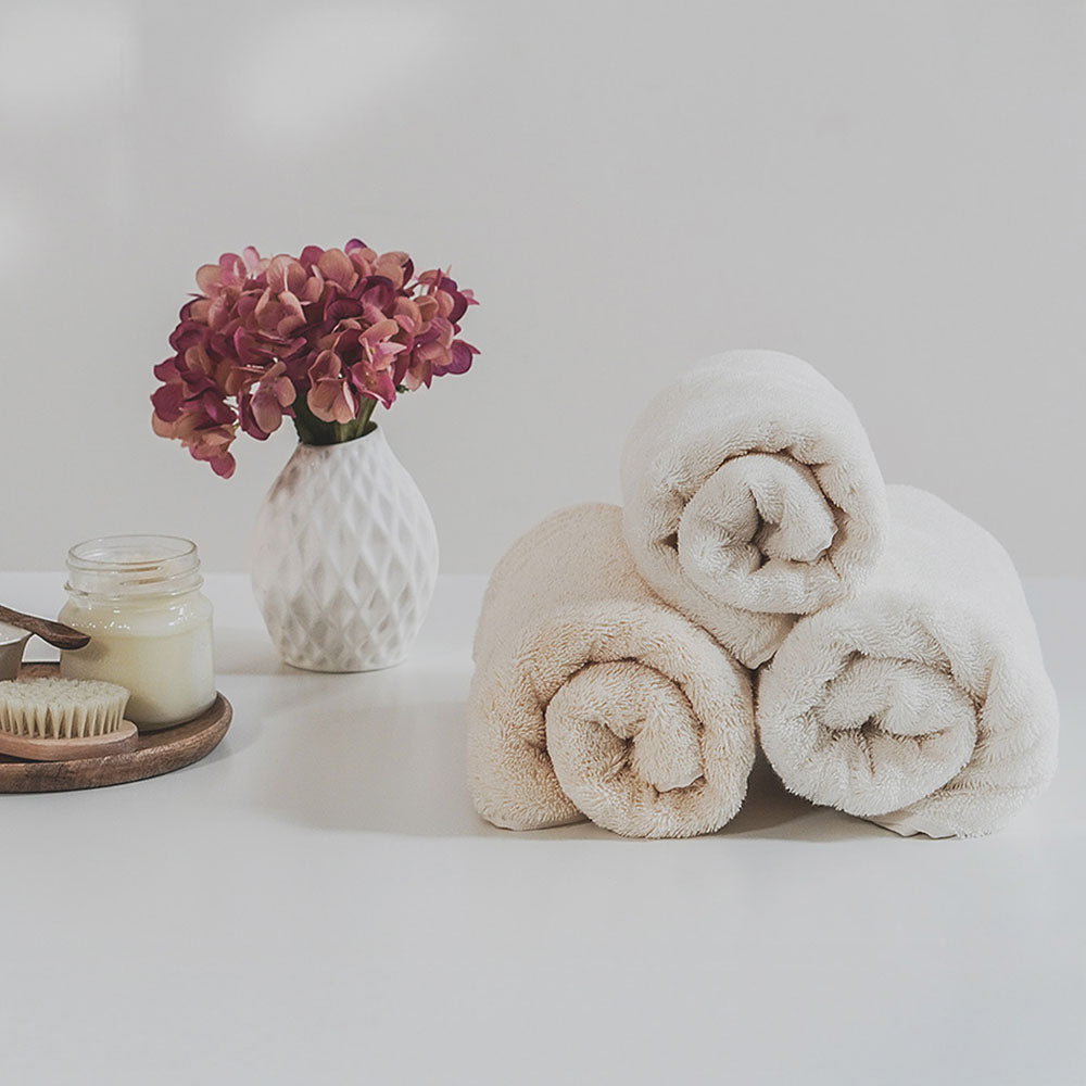 Drei gerollte Handtücher neben Vase mit Blumen und kleinem Holztablett.