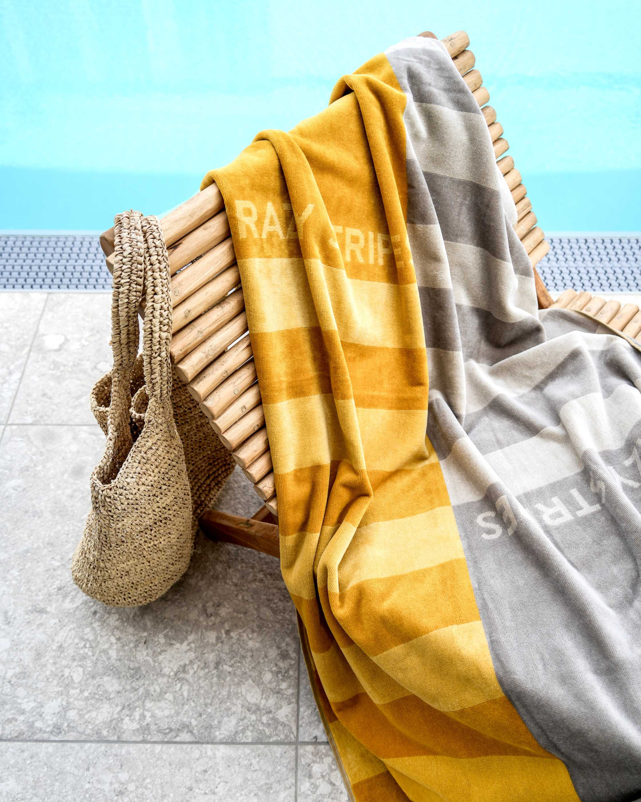 Gestreiftes Strandtuch auf Holzliege am Pool mit geflochtener Strandtasche