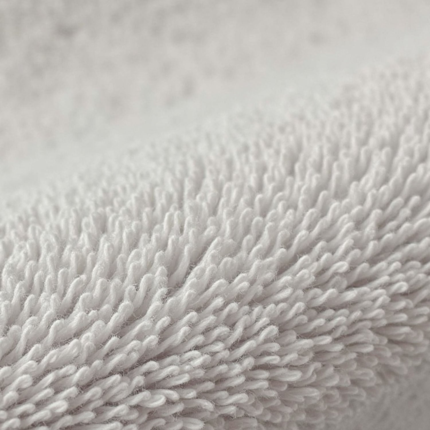 Detailreiche Ansicht der weichen, hochflorigen Schlingenstruktur eines weißen Handtuchs, die die flauschige Textur betont.