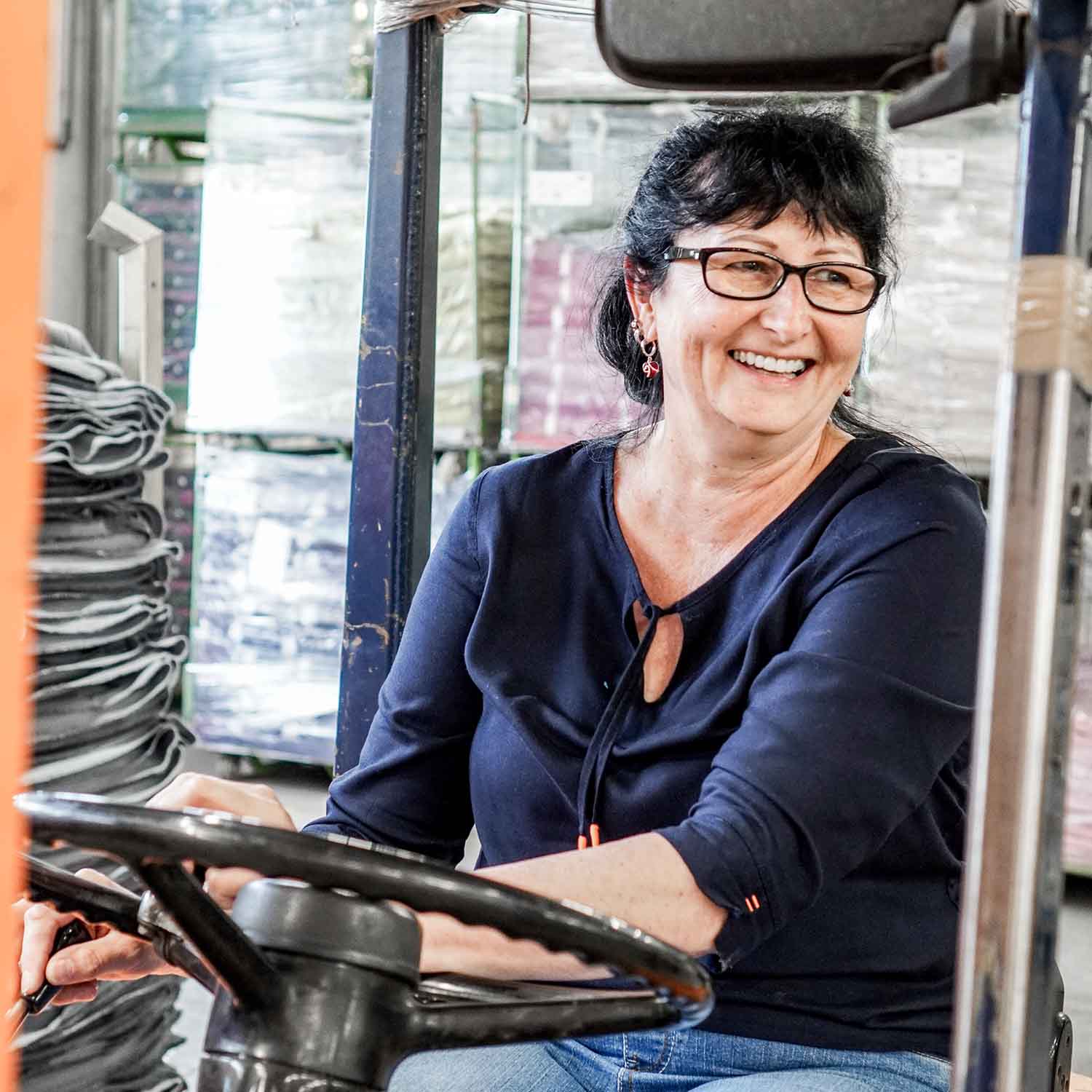 Nahaufnahme einer freundlichen Person fährt in einer Lagerhalle mit einem Stapler.
