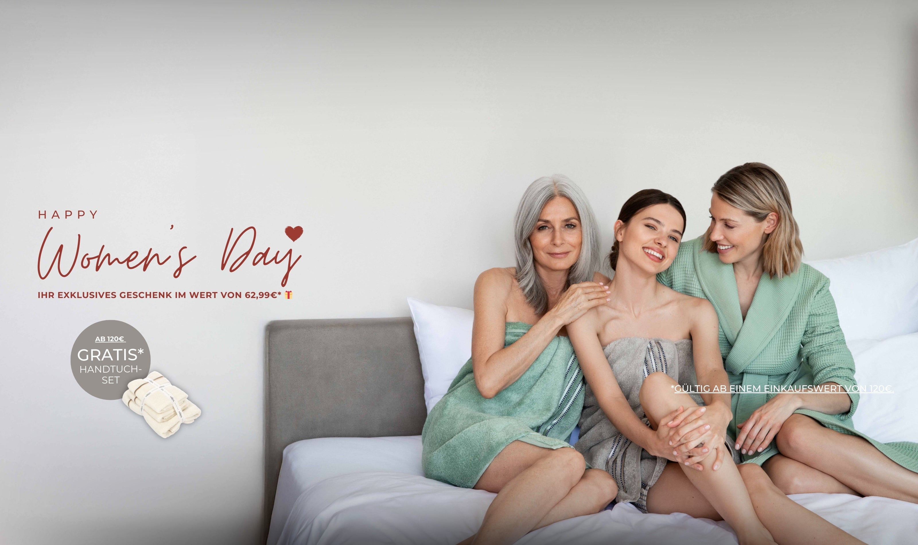 Drei Frauen in VOSSEN Bademänteln sitzen lächelnd auf einem Bett – Women’s Day Promotion mit exklusivem Geschenk und kostenlosem Handtuch-Set