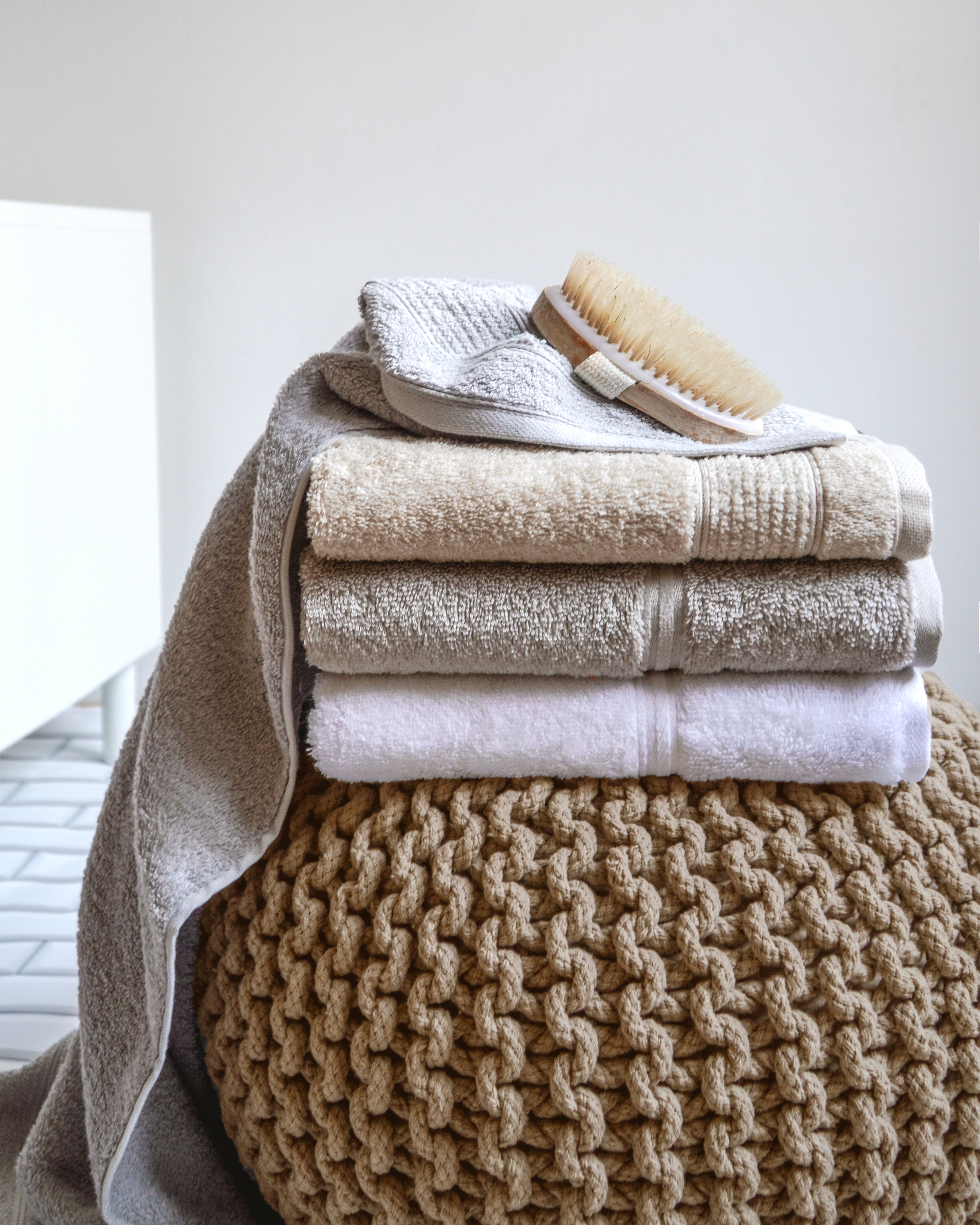 Gestapelte Handtücher mit Bürste auf gestricktem Pouf im Bad