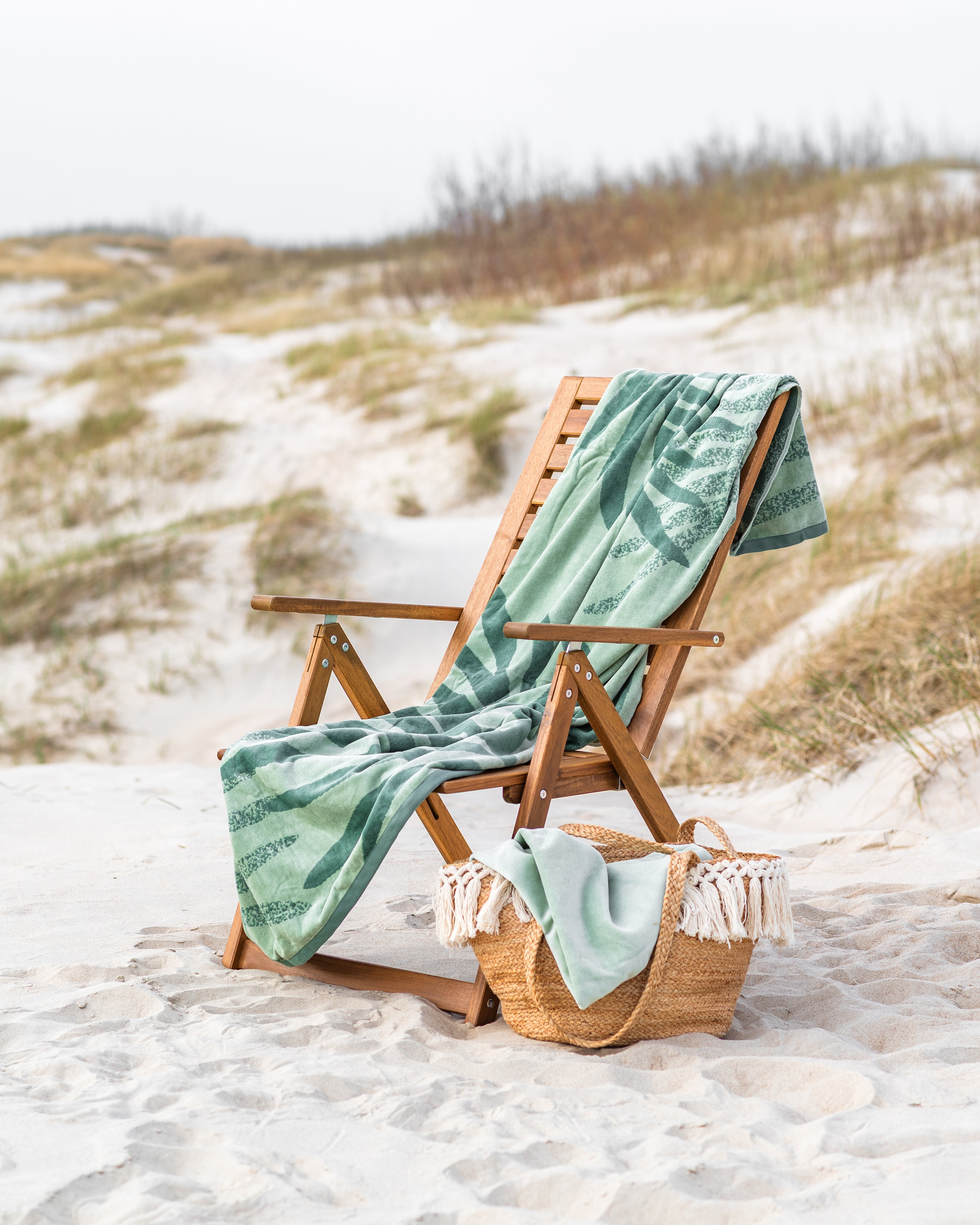 Strandtuch auf Liegestuhl in den Dünen mit Korbtasche am Strand