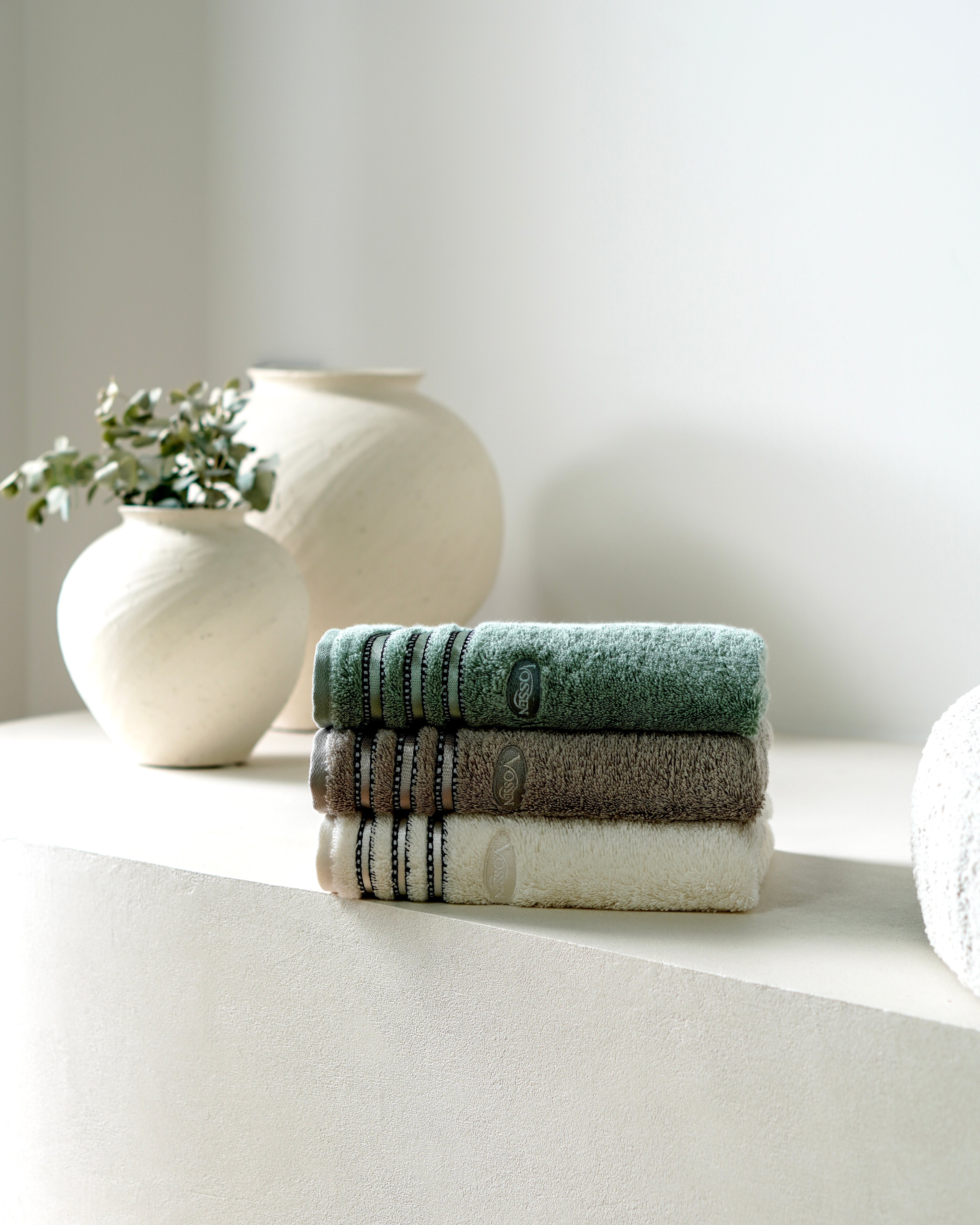 Gefaltete Handtücher in Naturtönen neben dekorativen Vasen