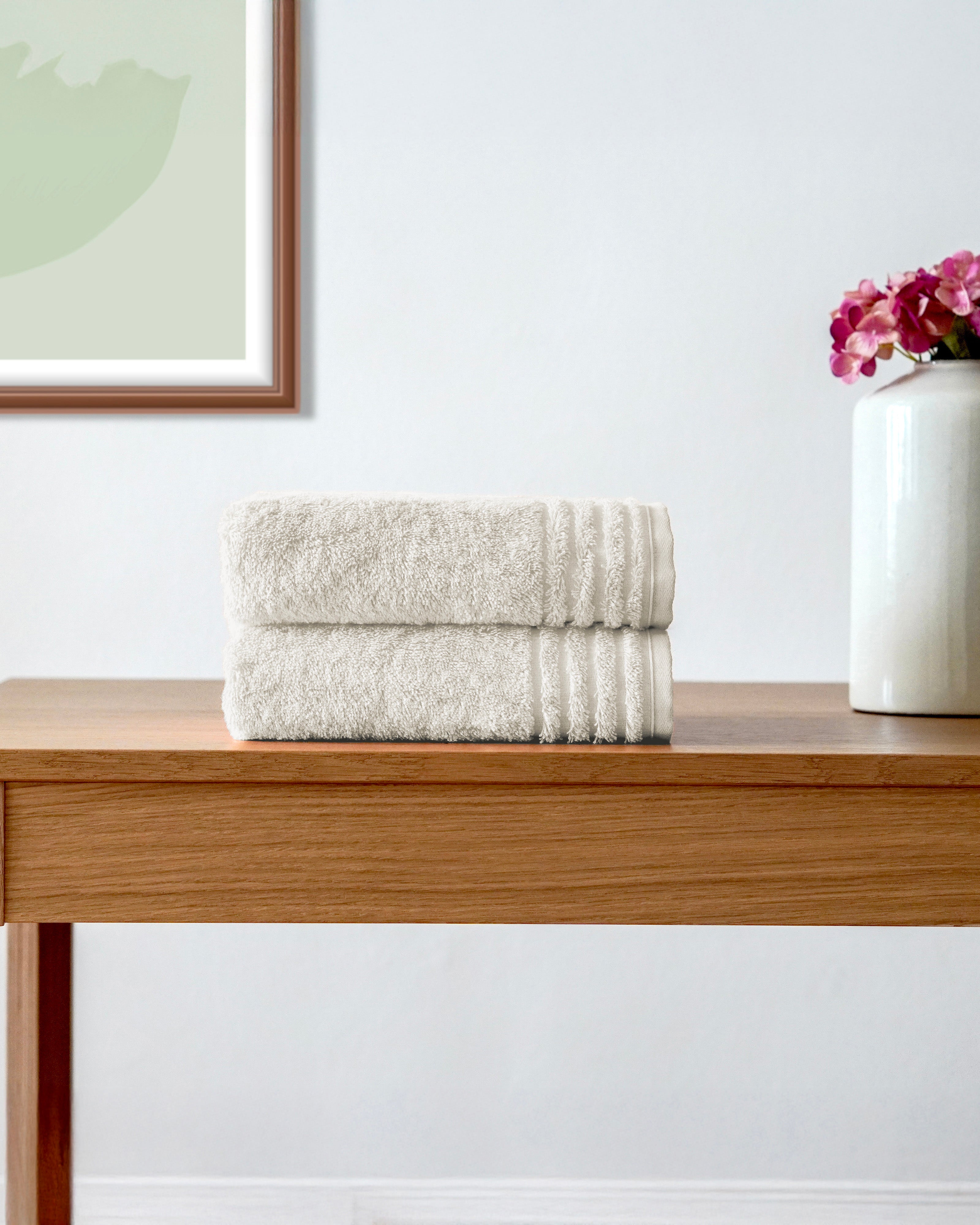 Zwei gefaltete Handtücher auf Holztisch neben Vase mit Blumen