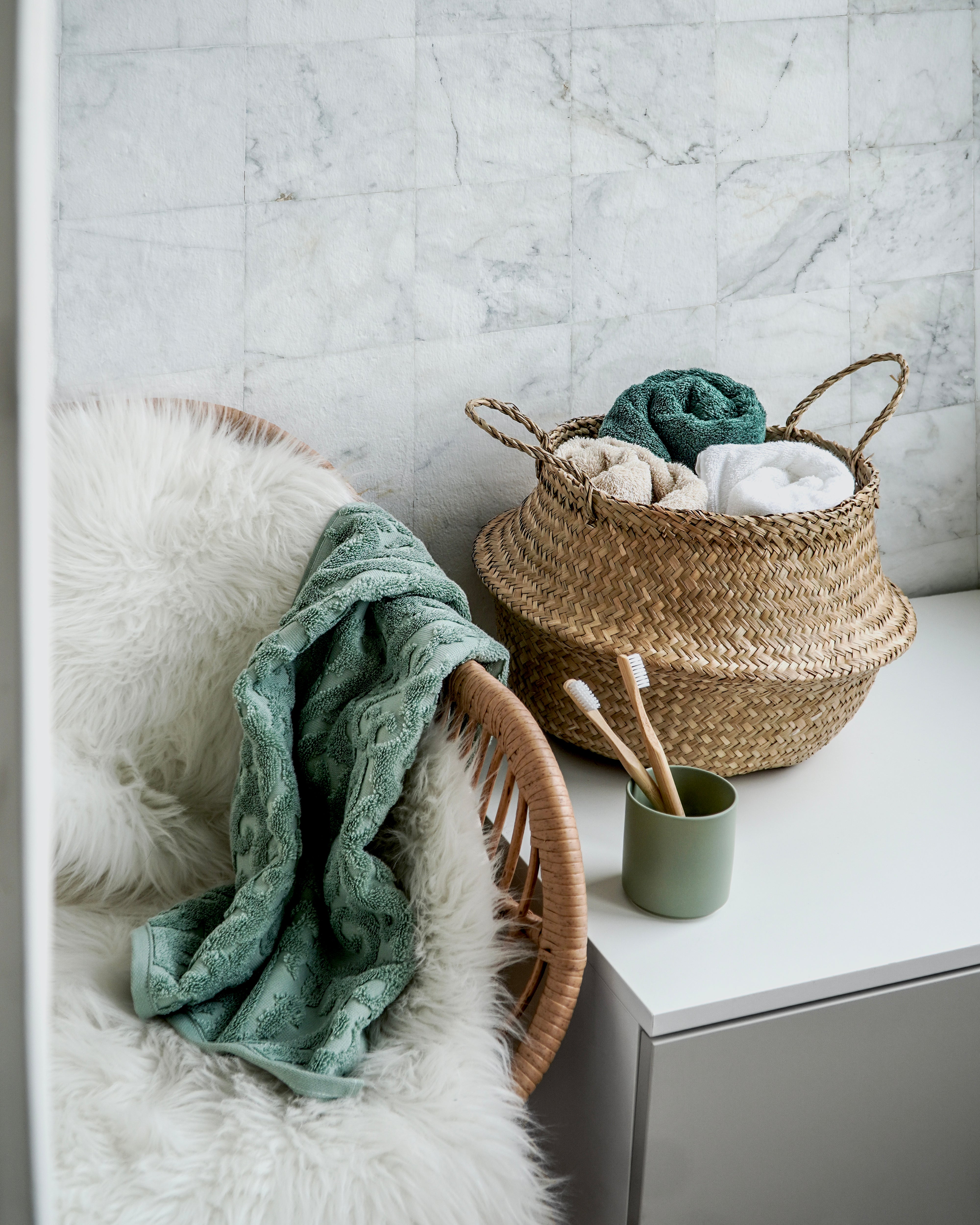 Geflochtener Korb mit Handtüchern neben Sessel und Badaccessoires