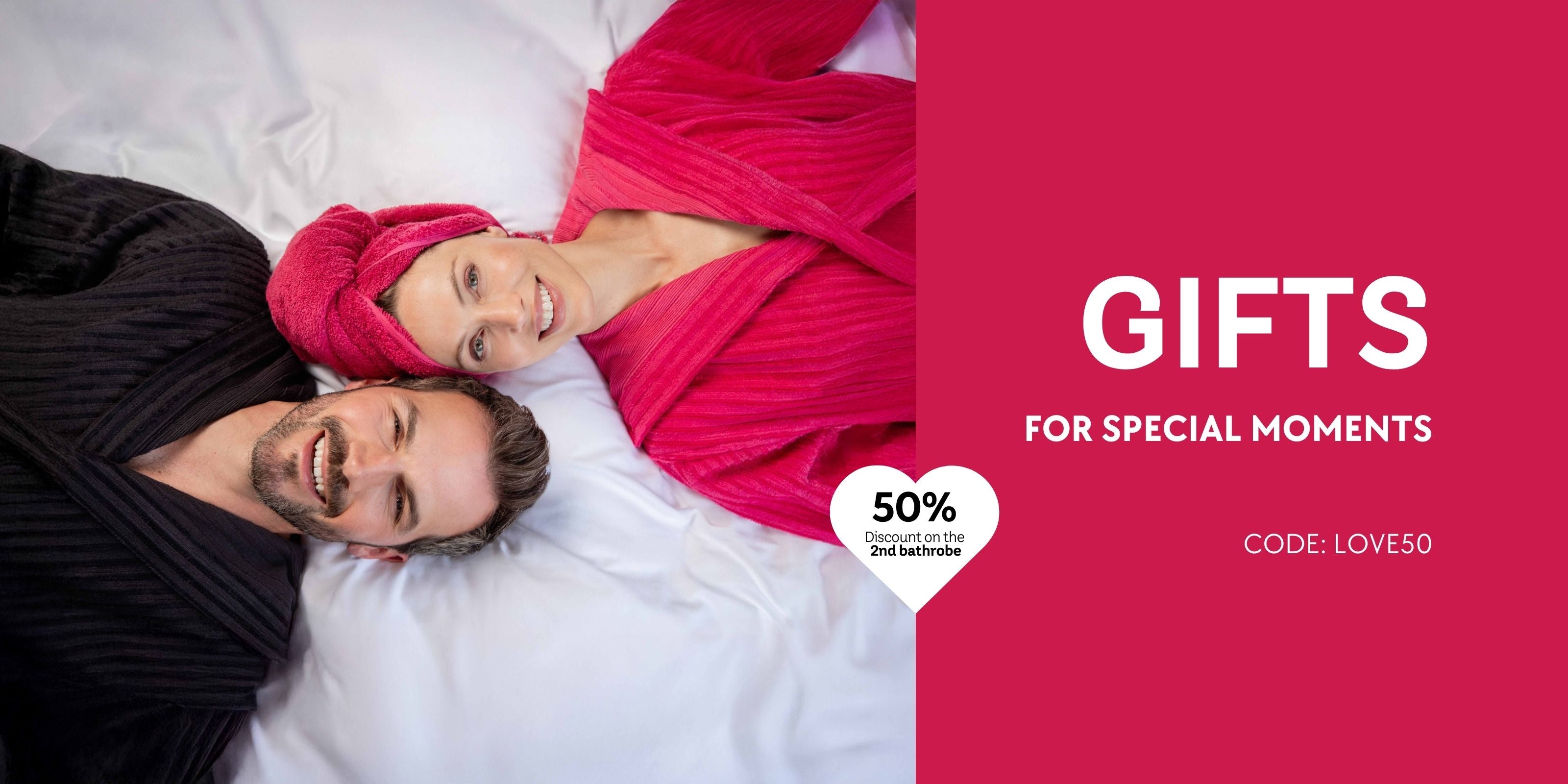 Paar in VOSSEN Bademänteln liegt entspannt auf weißer Bettwäsche, Geschenkaktion mit 50 % Rabatt auf den zweiten Bademantel – Geschenkideen für besondere Momente.