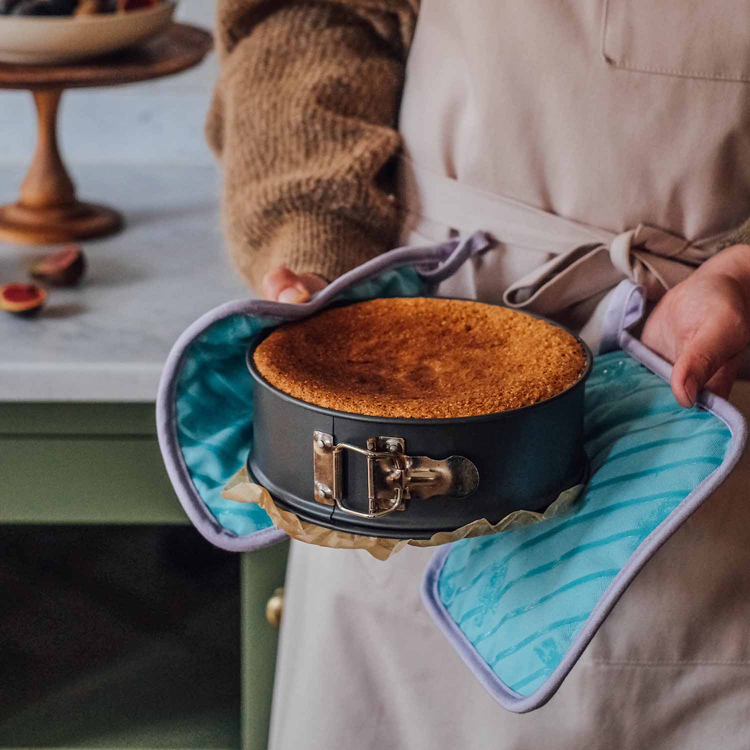 Frisch gebackener Kuchen in einer Springform, gehalten mit Ofenhandschuhen in der Küche – goldbrauner Kuchen nach dem Backen