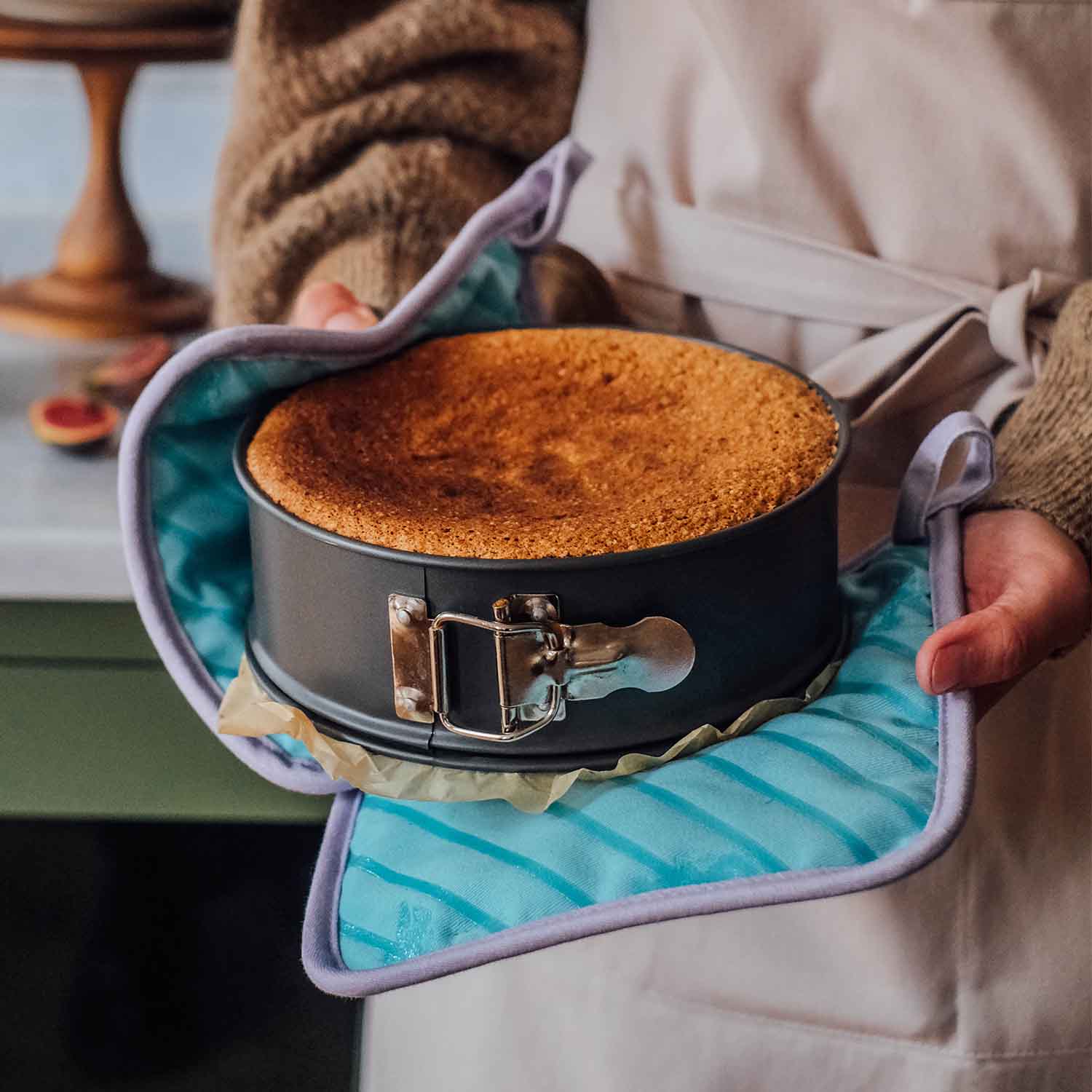 Frisch gebackener Kuchen in einer Springform, gehalten mit Ofenhandschuhen in der Küche – goldbrauner Kuchen nach dem Backen