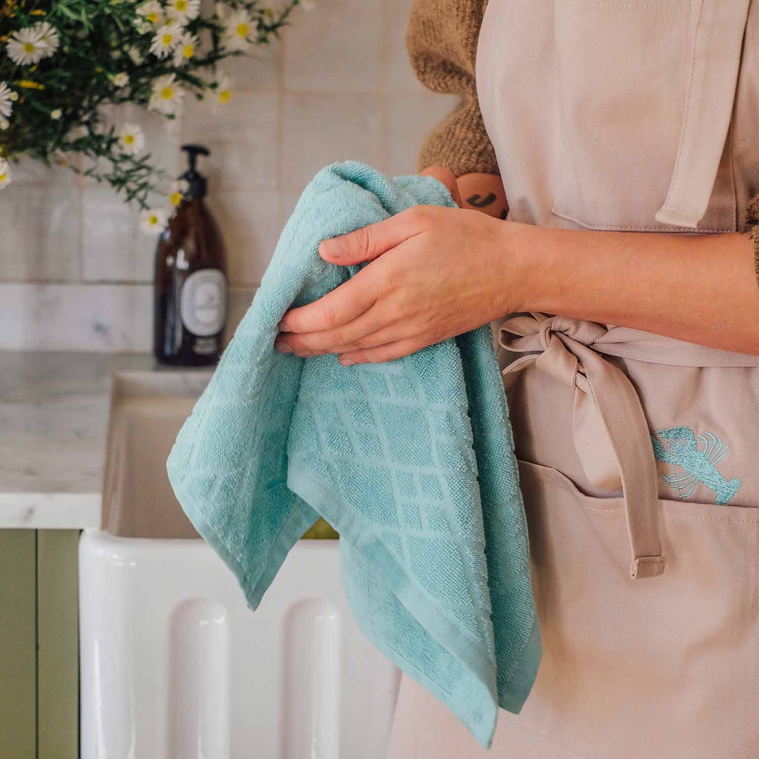Küchenhelferin mit mintgrünem Geschirrtuch aus Baumwolle in moderner Küche mit Blumen und Seifenspender