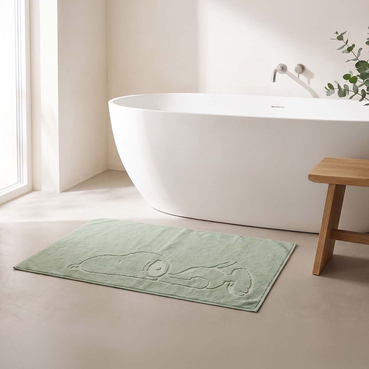 Hellgrüne Badematte mit eingeprägtem Snoopy-Motiv vor einer freistehenden weißen Badewanne in einem hellen, minimalistisch eingerichteten Badezimmer.