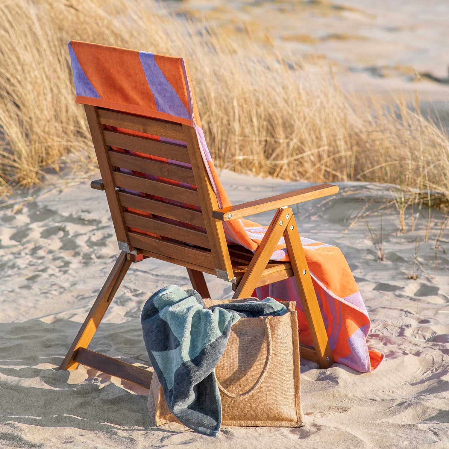 Buntes Strandtuch auf Holzliegestuhl mit Strandtasche in den Dünen
