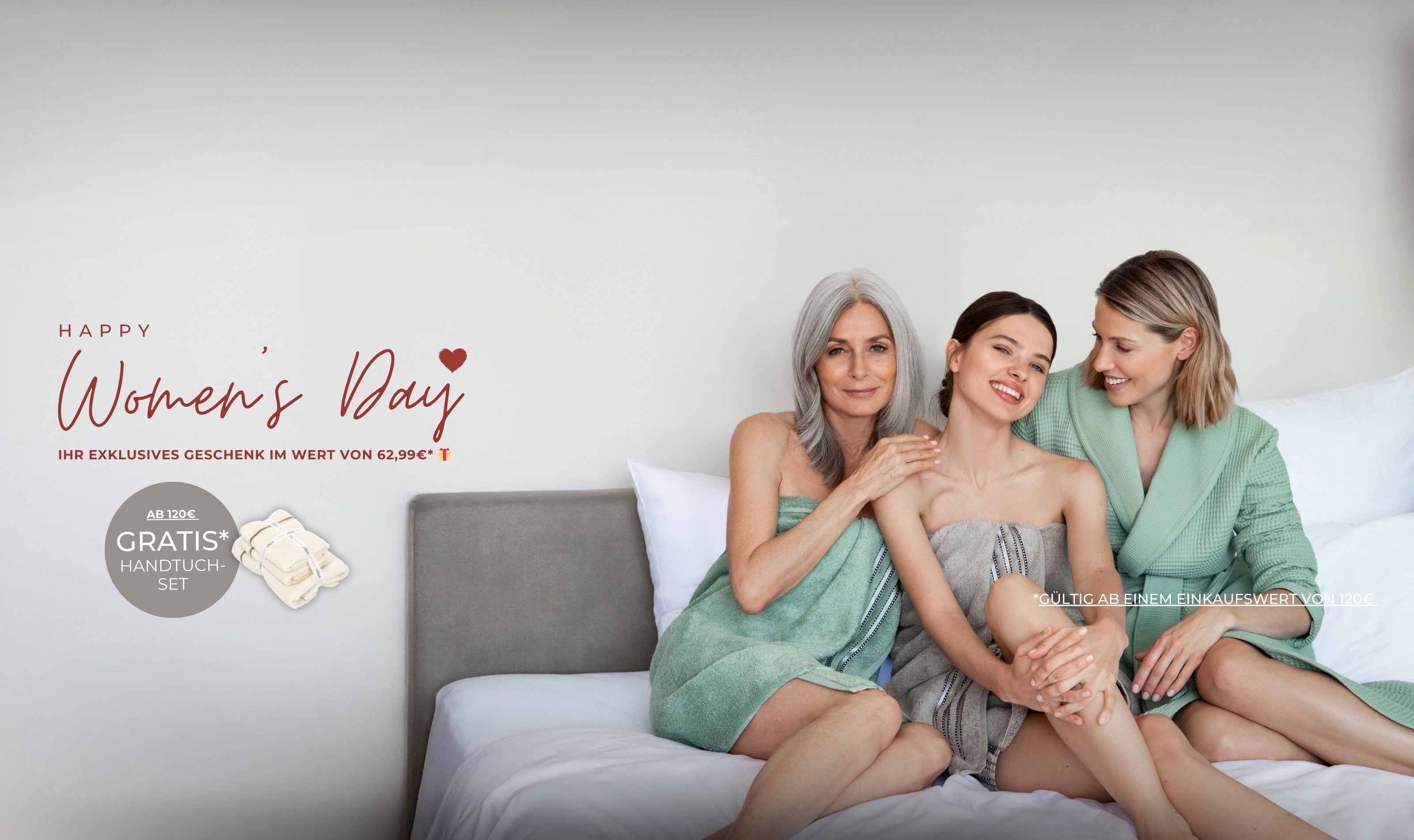 Drei Frauen in VOSSEN Bademänteln sitzen lächelnd auf einem Bett – Women’s Day Promotion mit exklusivem Geschenk und kostenlosem Handtuch-Set