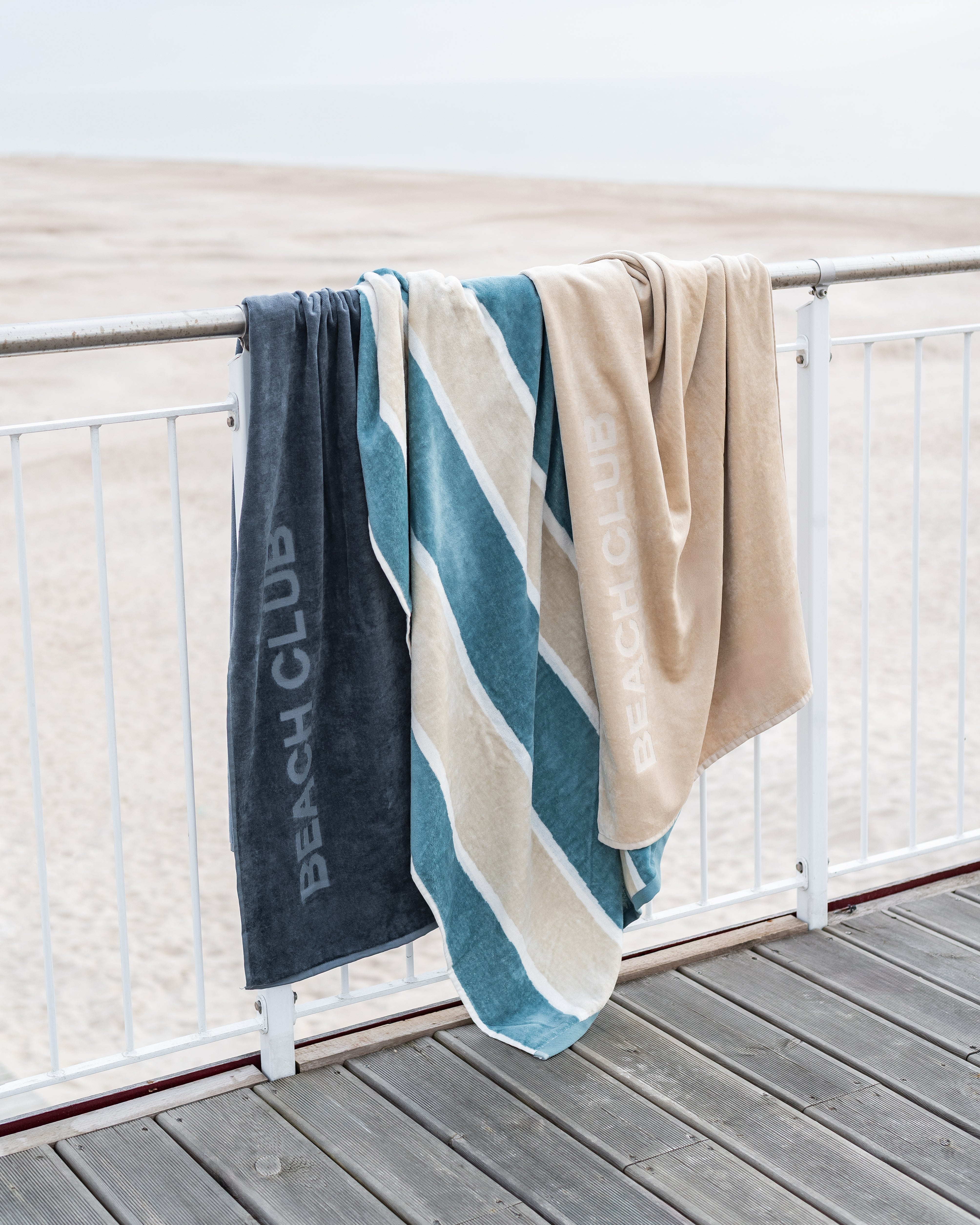 Strandtücher in Blau- und Naturtönen am Geländer mit Blick auf den Strand